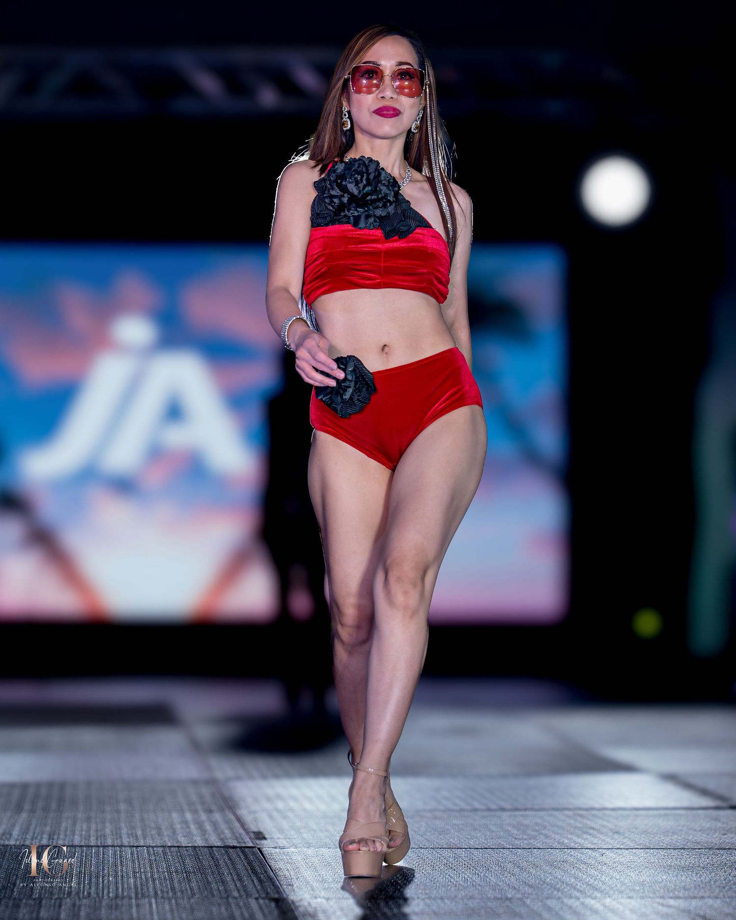 Models showcase swimwear collection on illuminated runway during fashion show with dramatic lighting effects.