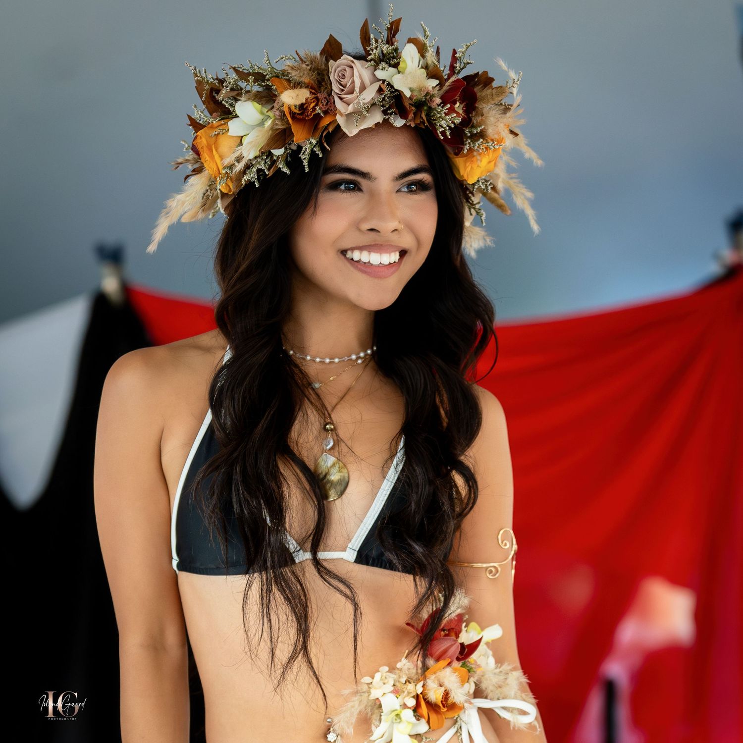 Model wearing floral crown poses outdoors with red backdrop.