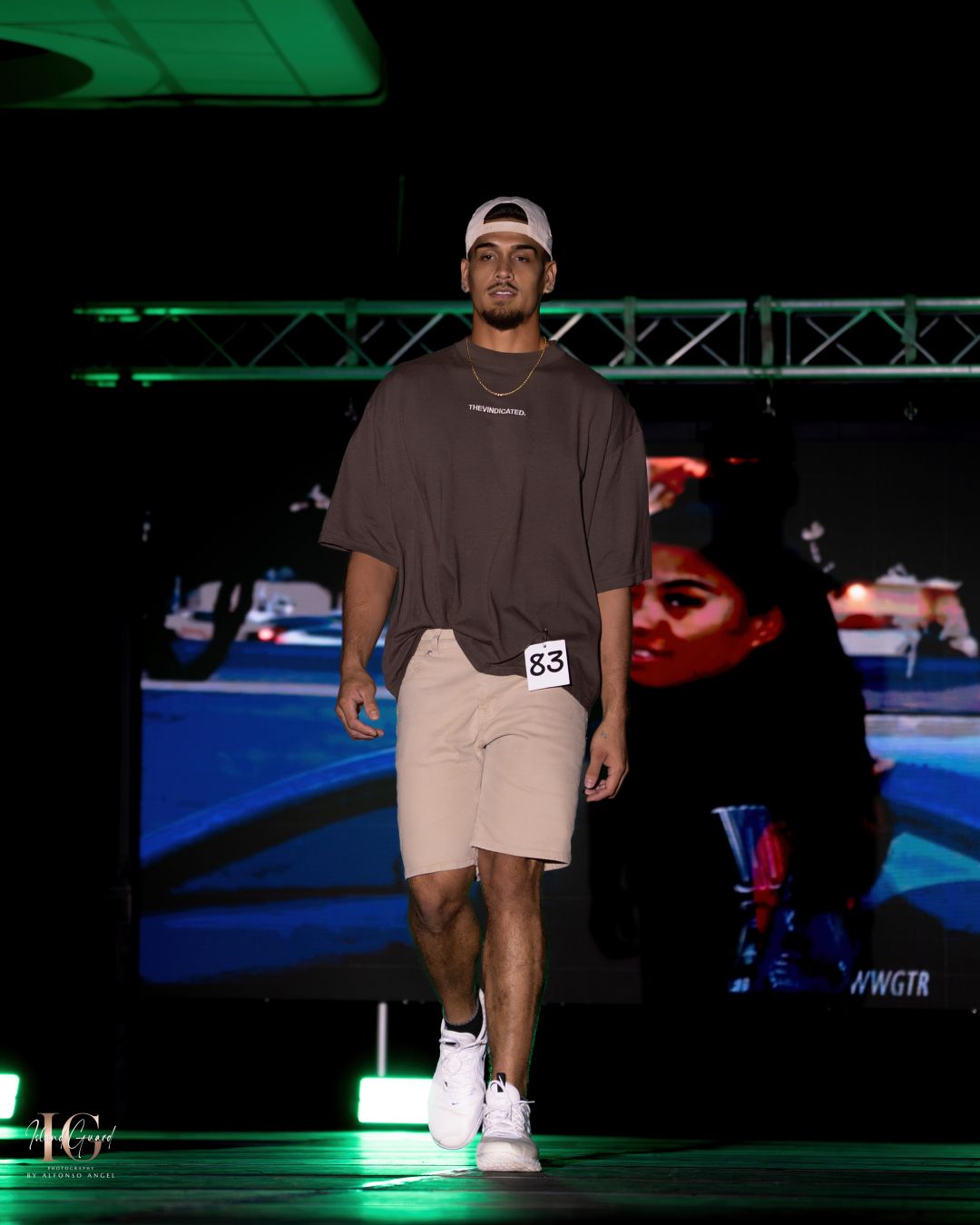 Male model walks runway in casual brown t-shirt and khaki shorts combination.