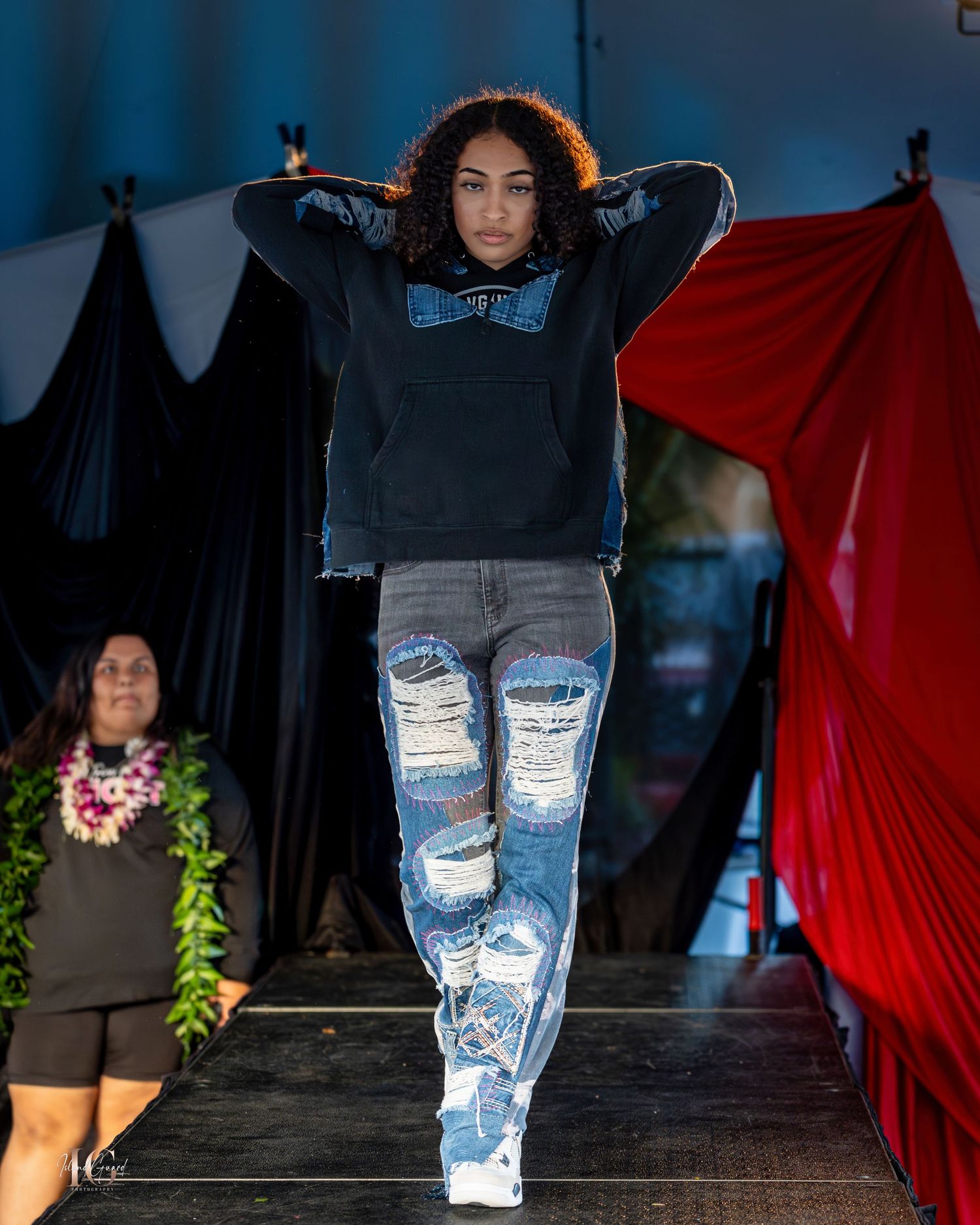 Model wearing distressed denim jeans and hoodie on fashion runway.