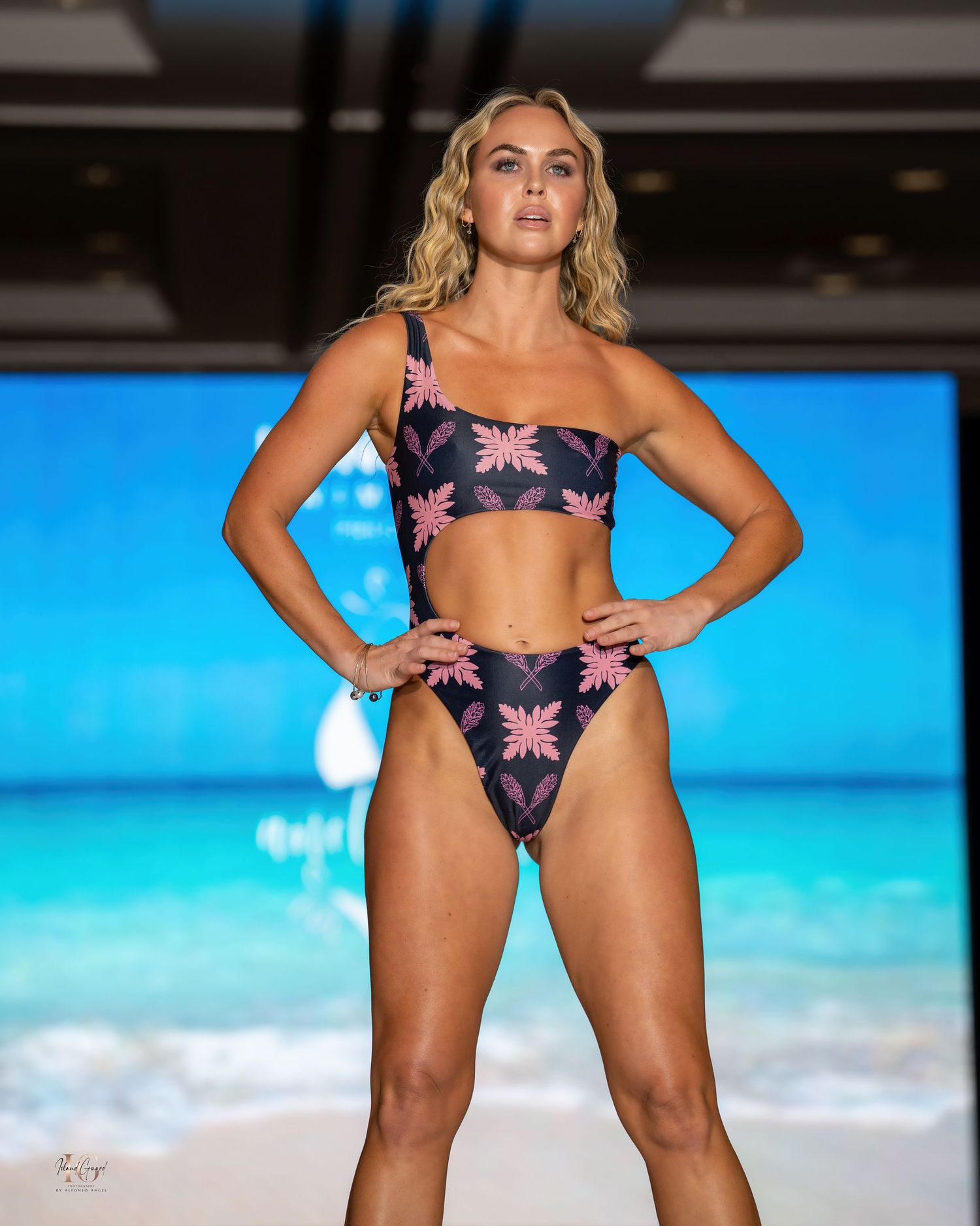 Fashion model poses in dark floral two-piece swimsuit during tropical-themed swimwear show.