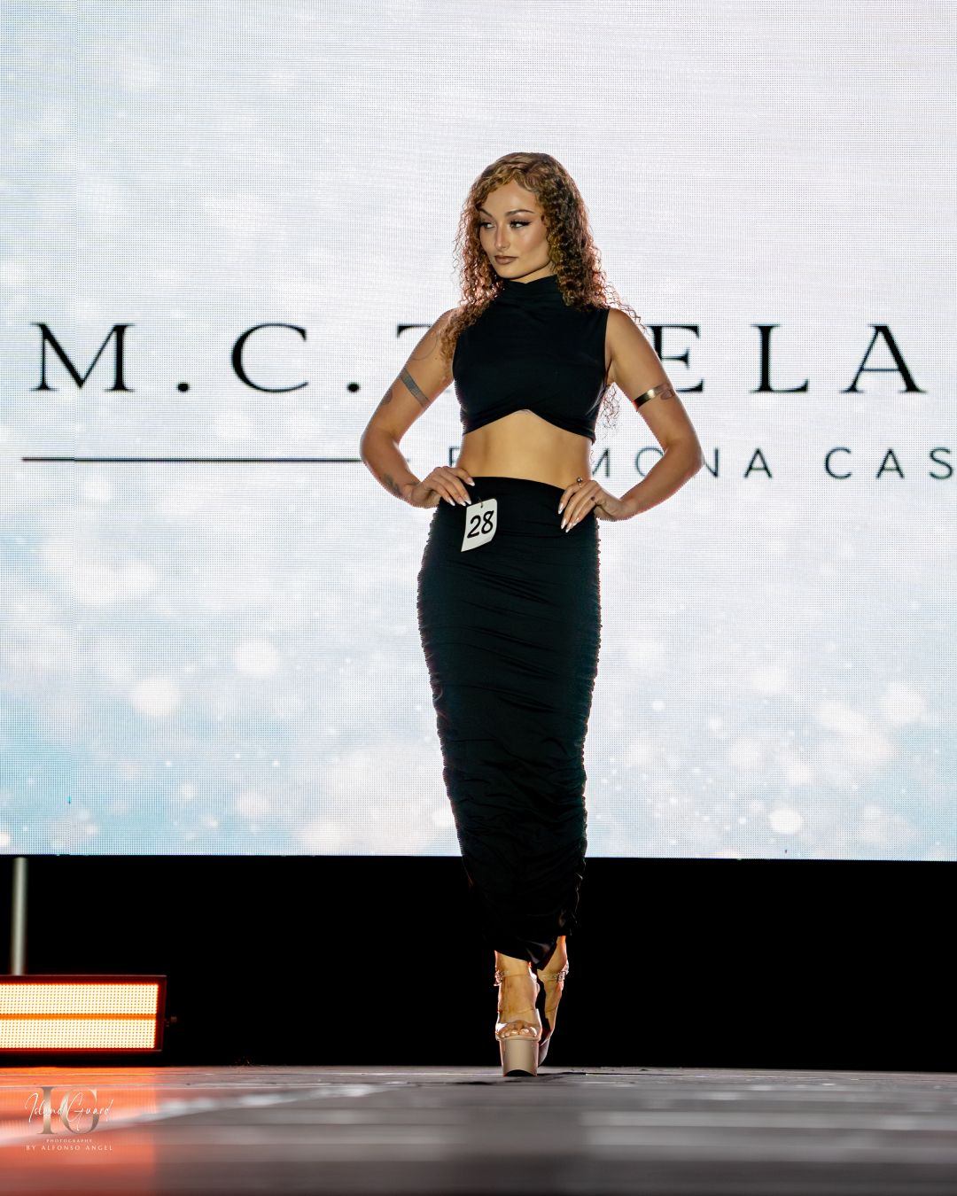 Model presents black crop top and pencil skirt ensemble on fashion runway.
