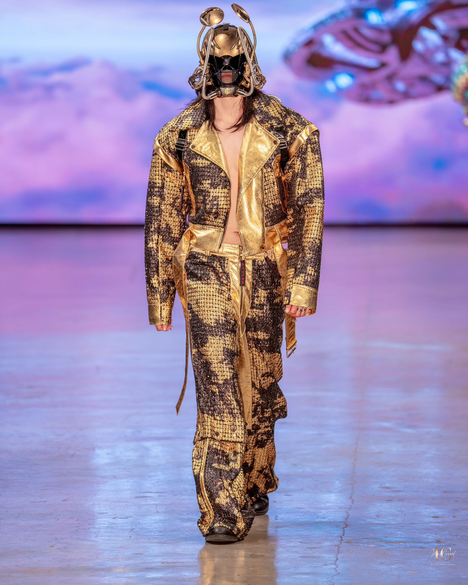 Fashion model walks runway in brown and gold metallic camouflage print oversized coat during fashion show.