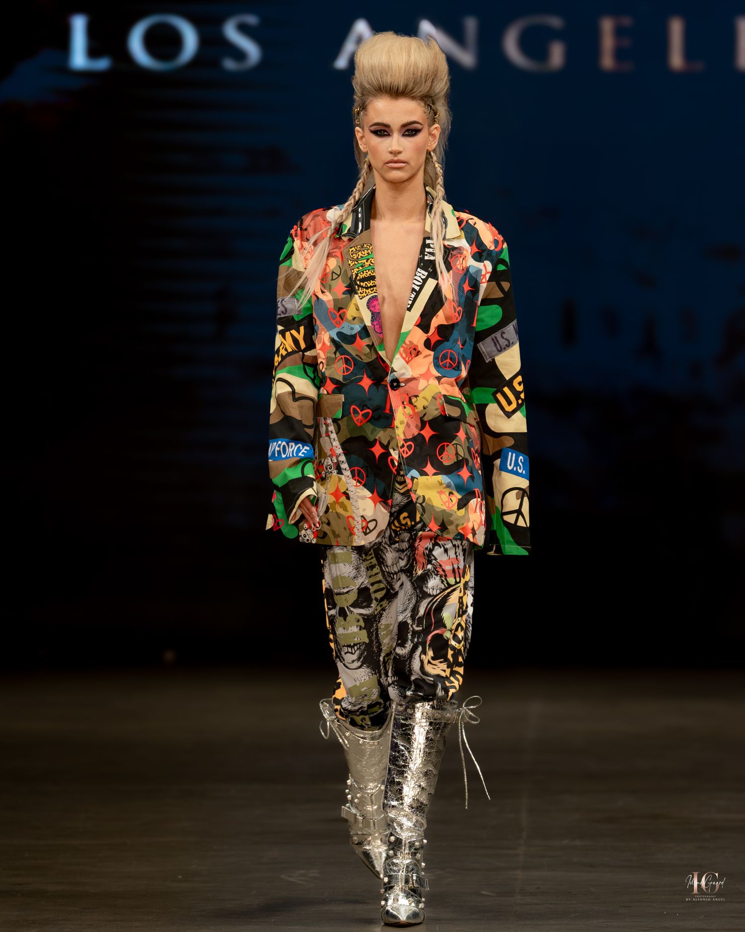 Model walks runway in floral print blazer and metallic silver boots at Los Angeles fashion show.
