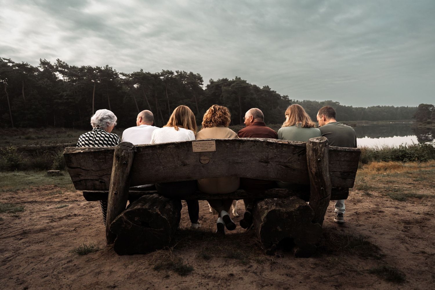 People sit on rustic wooden benches overlooking a scenic mountain landscape at sunset.