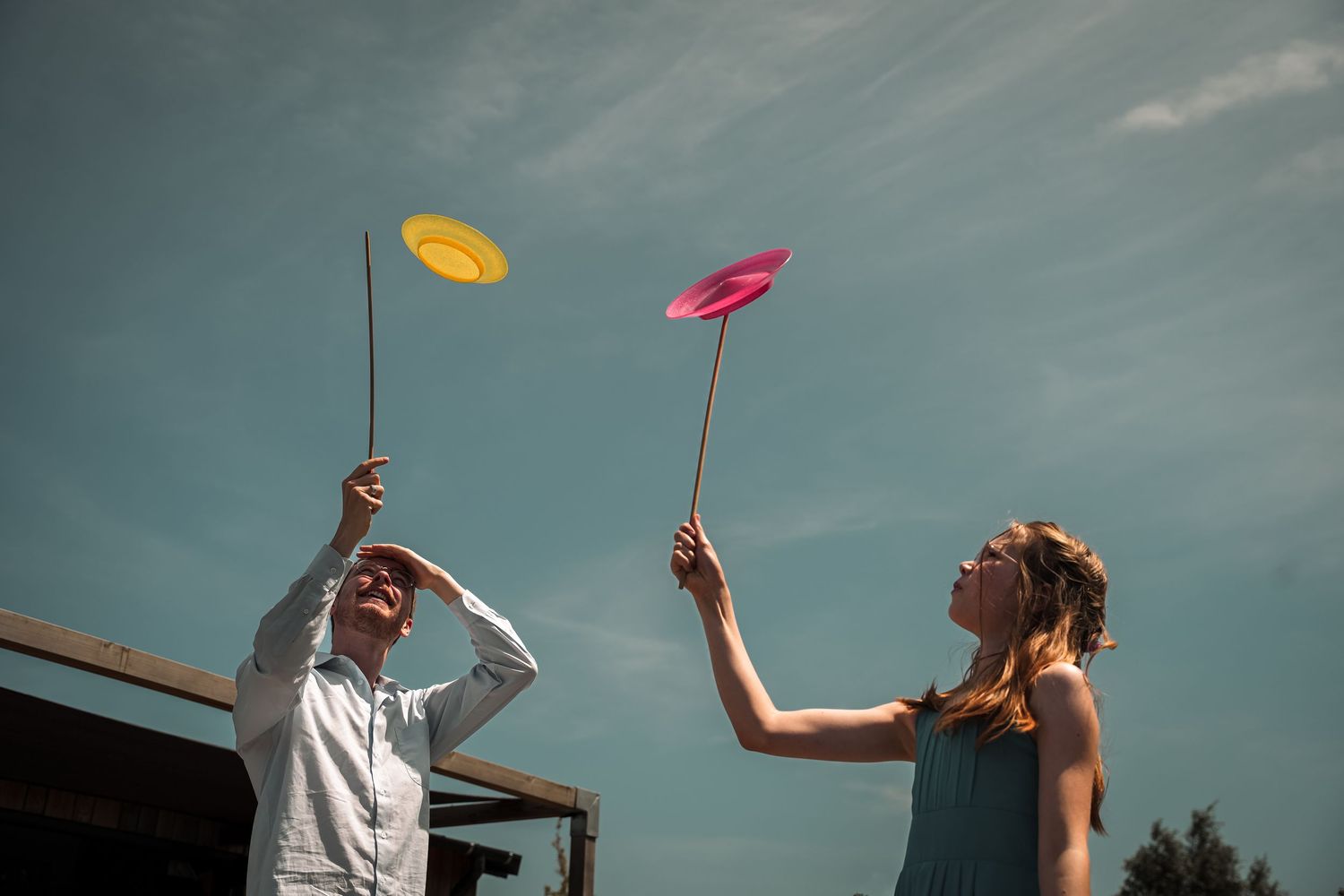 A person in white and another in black play catch with colorful flying discs against a blue sky background.