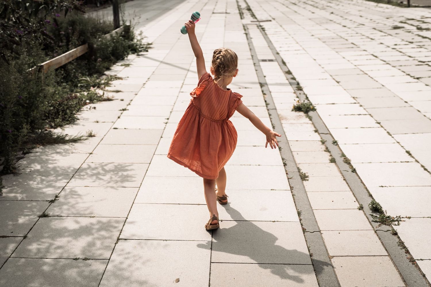 Small child in an orange dress running along a stone pathway.