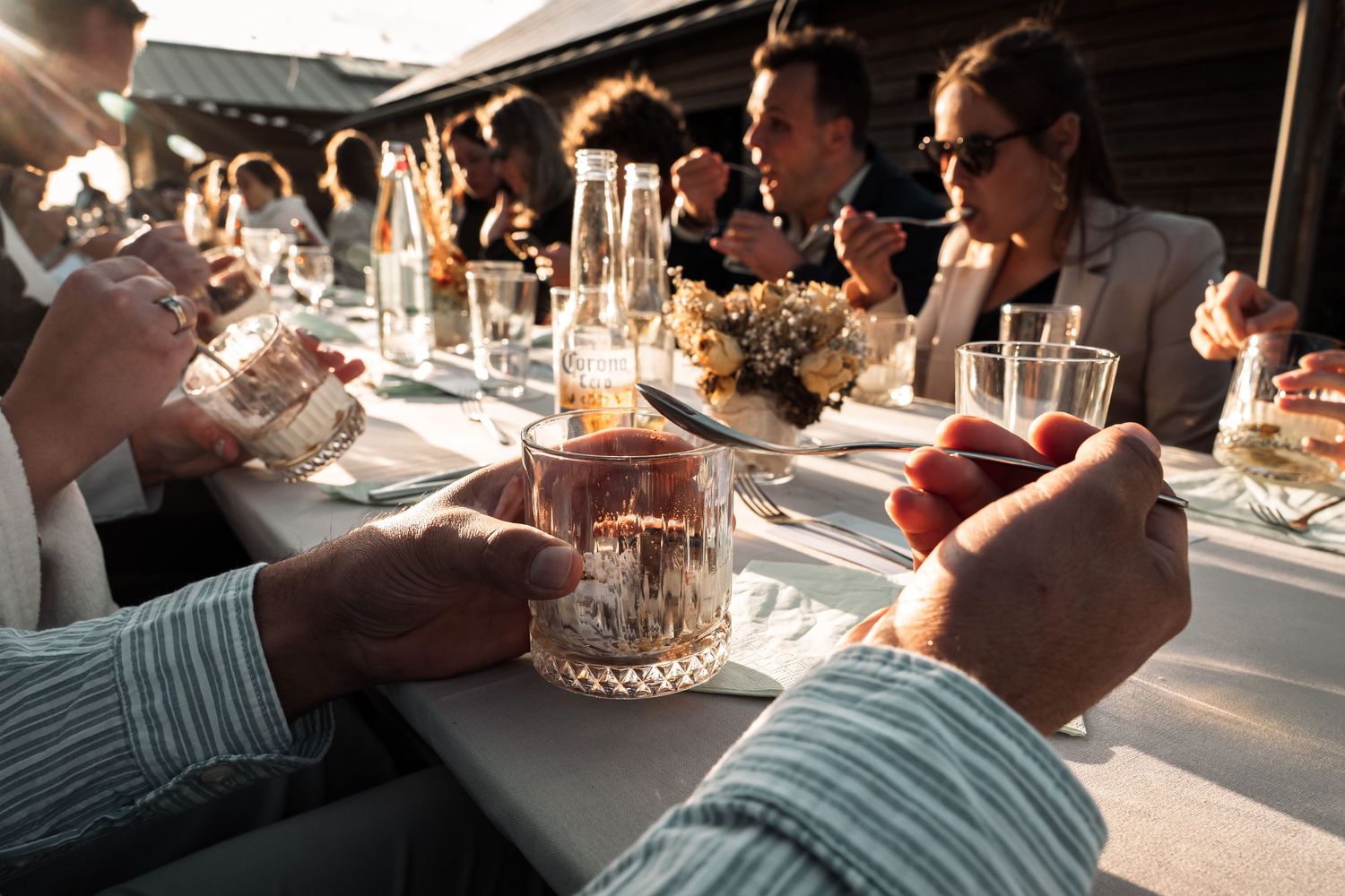 People enjoying drinks and conversation at an outdoor dinner party table during golden hour.