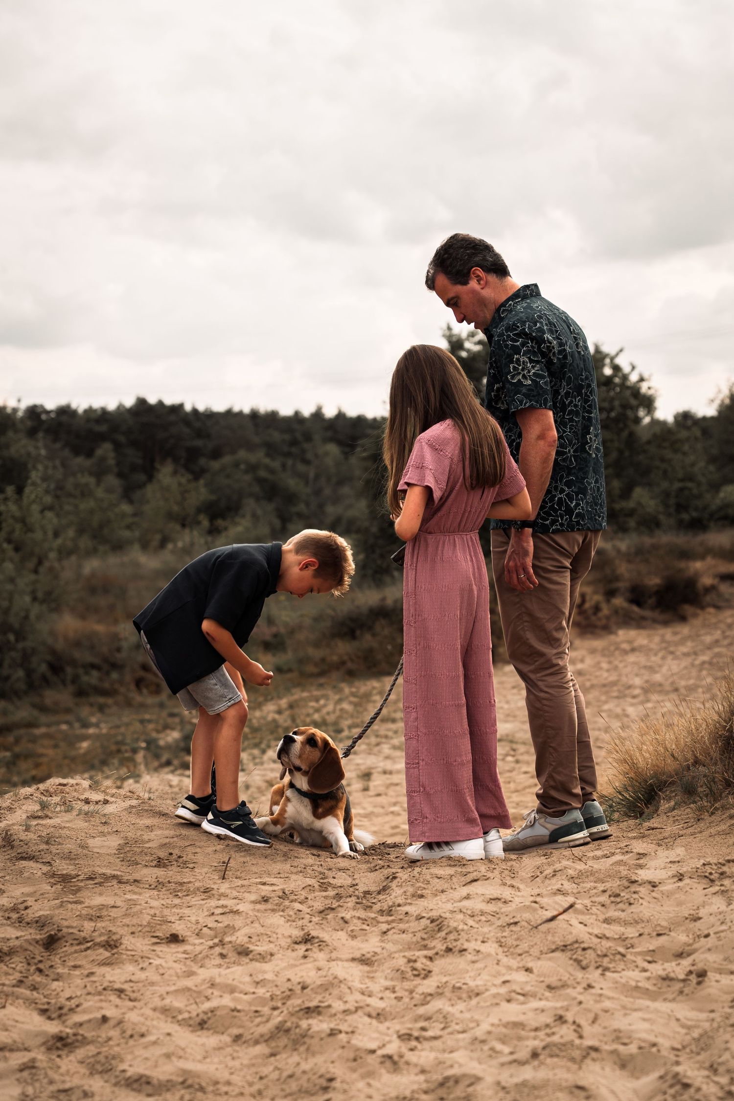 A family stands together on a sandy hill with their dog in a series of candid outdoor moments.