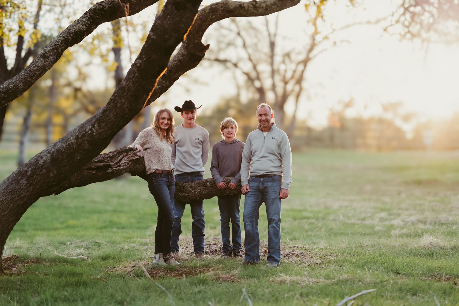 Family group standing together under a large tree branch at sunset in a park setting.