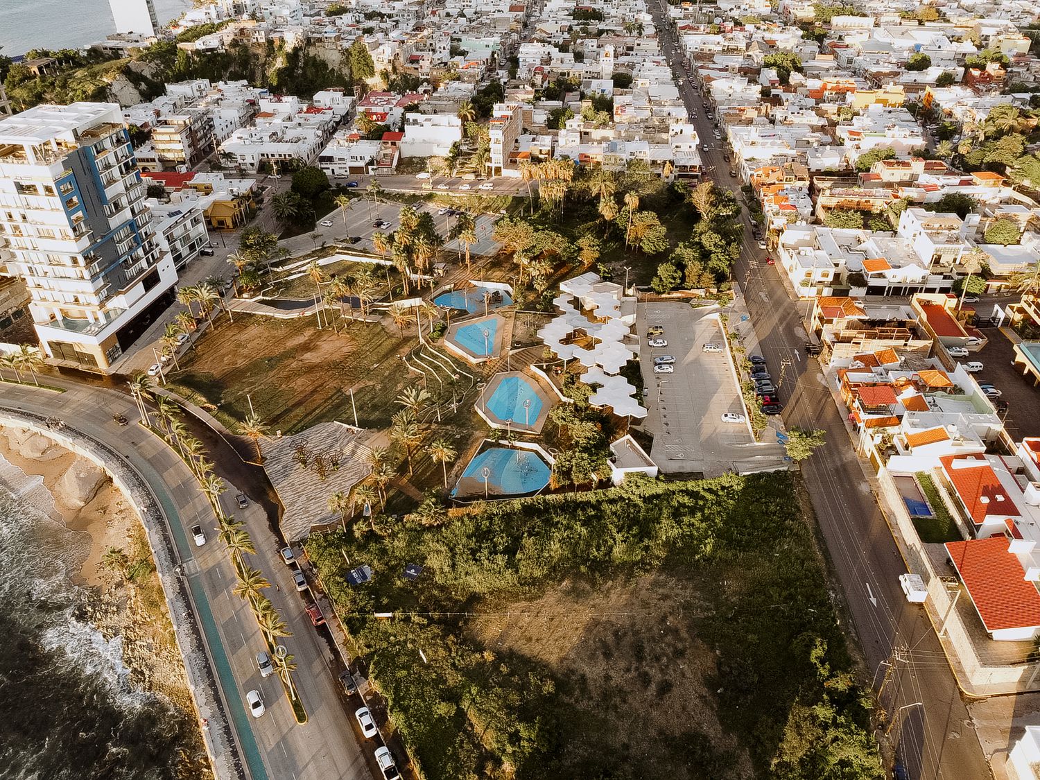 Aerial drone shot shows cars winding down a hilly neighborhood street with tightly packed houses on both sides.