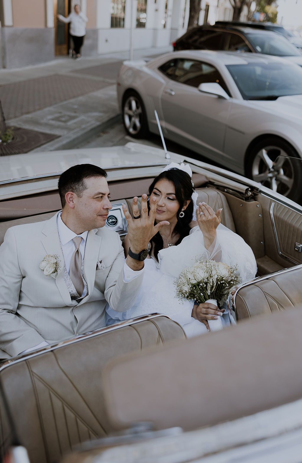 Happy couple shares romantic candid moments in vintage car during wedding photoshoot.
