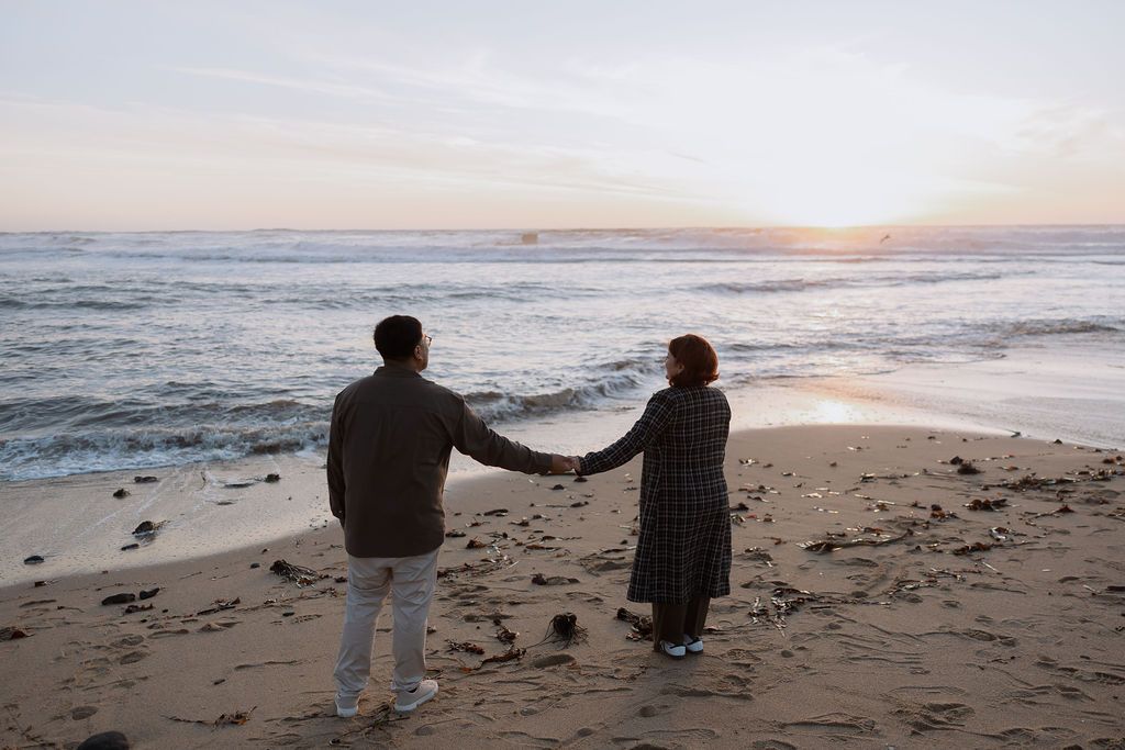 Silhouettes of people walking together on a sandy beach at sunset while holding hands.