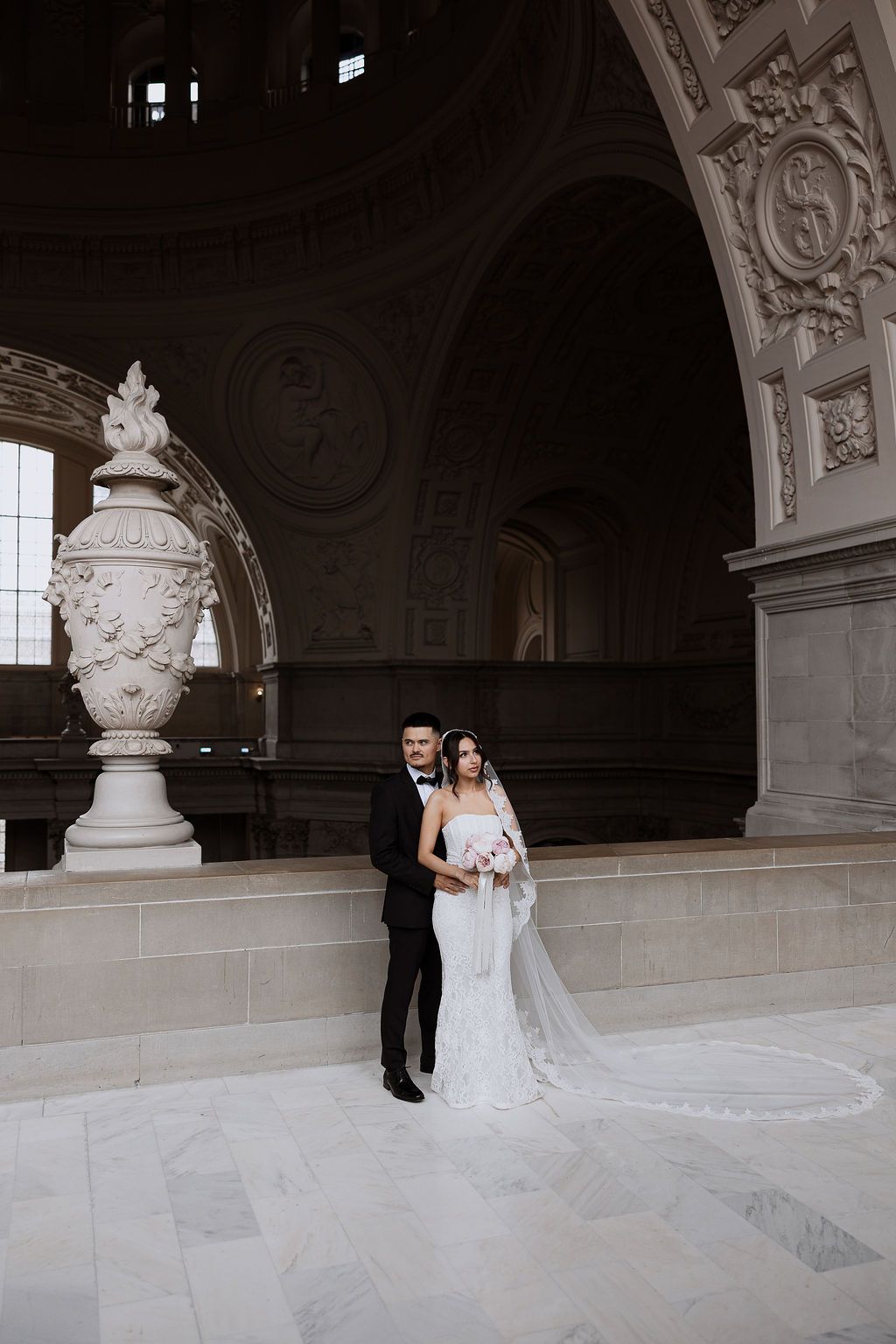A classic wedding couple poses for portraits in an elegant marble hall with ornate architectural details and decorative urns.