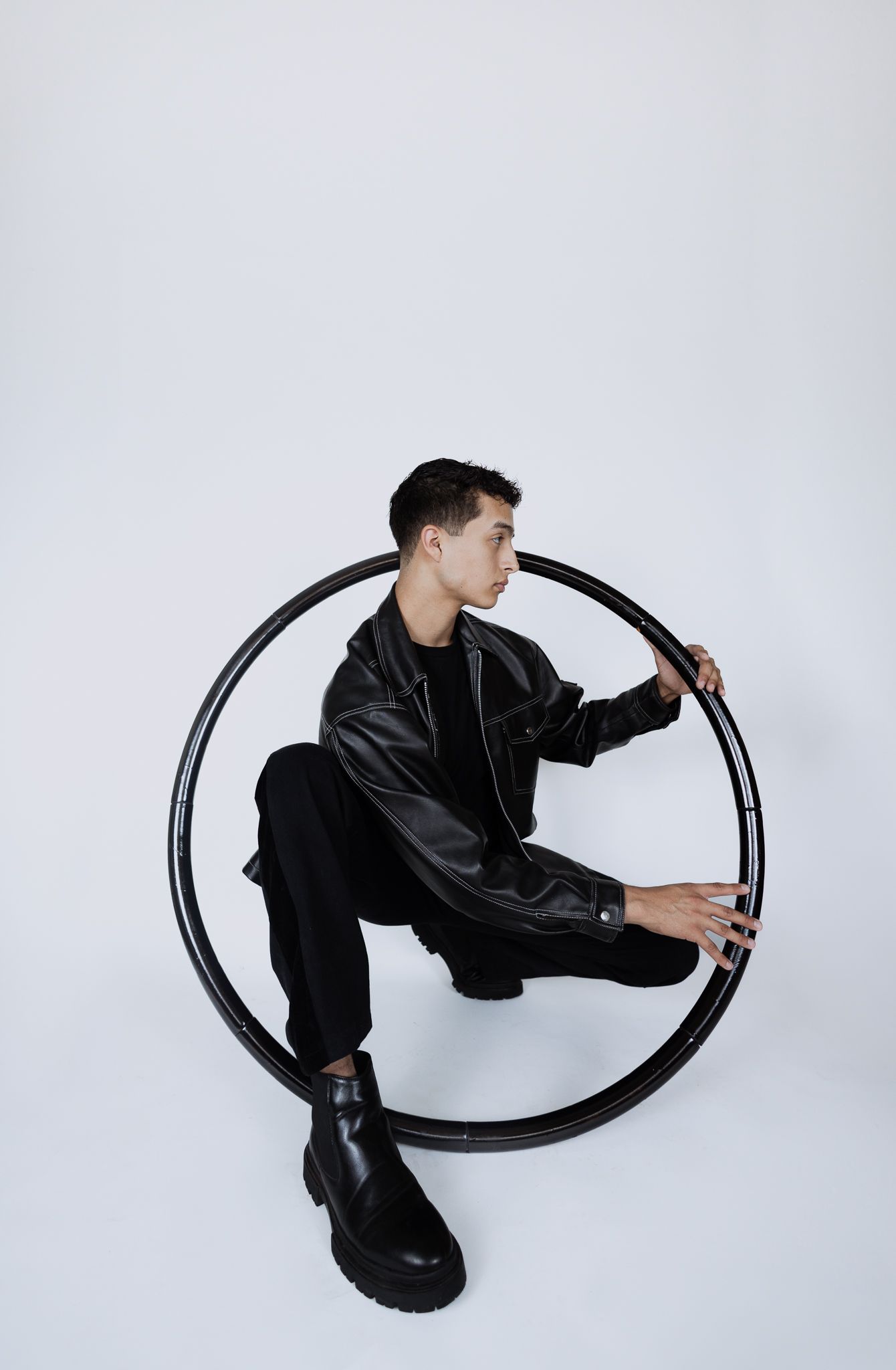 Artistic studio photoshoot featuring person in black leather jacket interacting with circular metal frame in four poses.