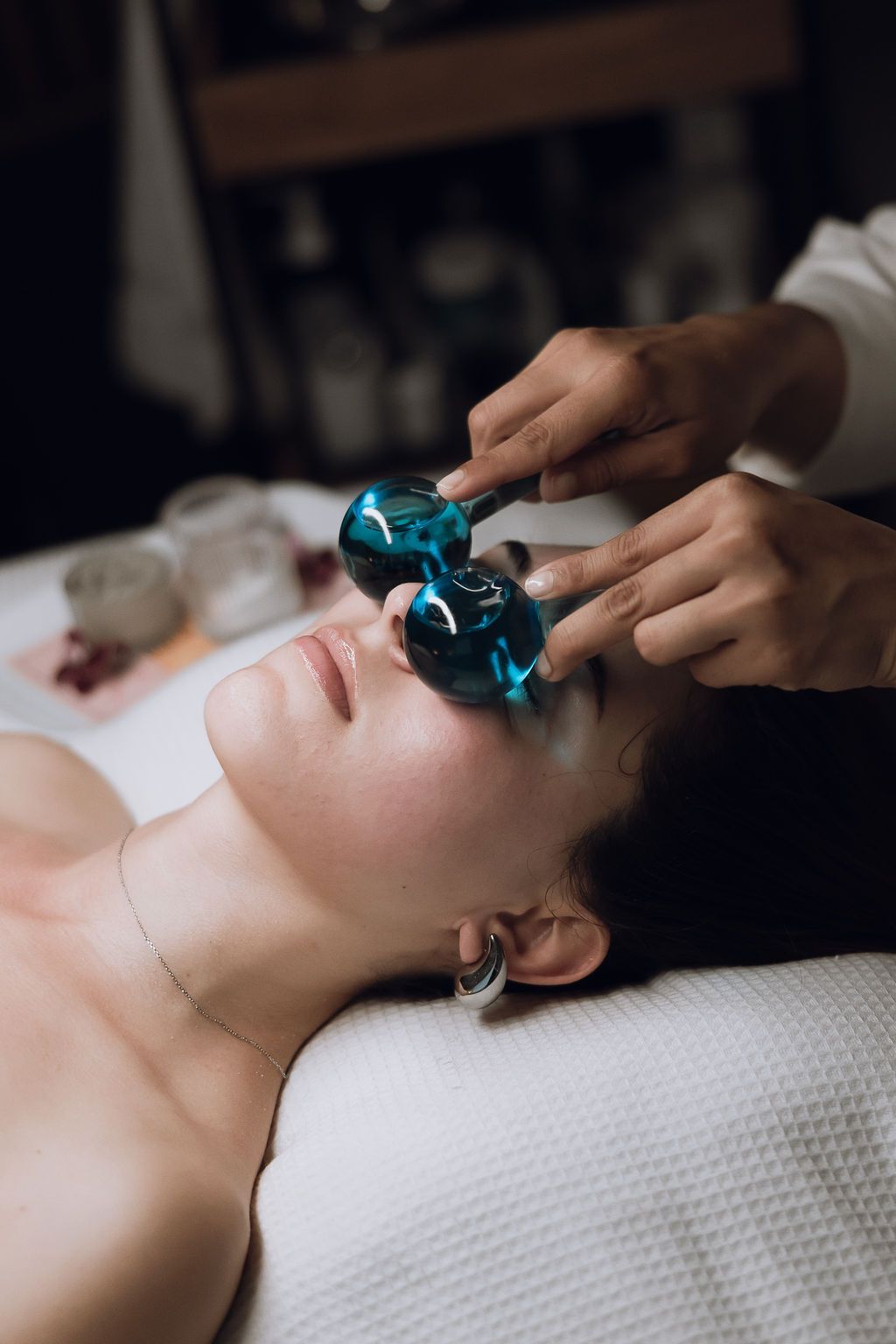 Blue crystal facial rollers being used during a luxurious spa treatment on white textured surface.