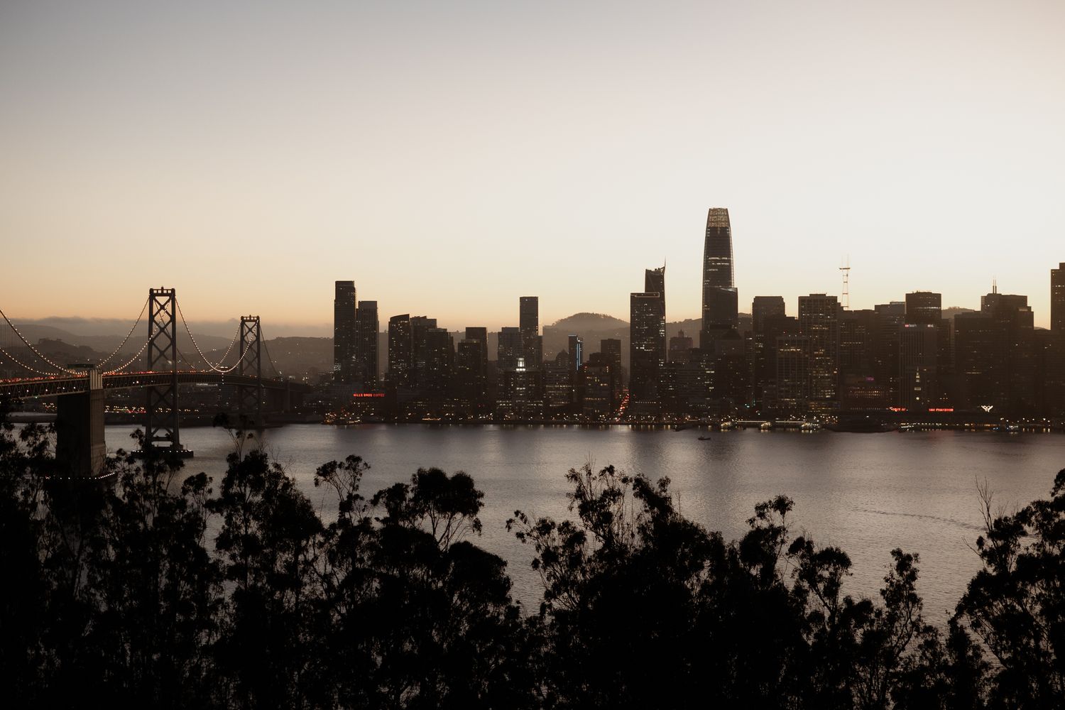 San Francisco skyline at dusk with Bay Bridge and downtown skyscrapers silhouetted against golden sunset sky.