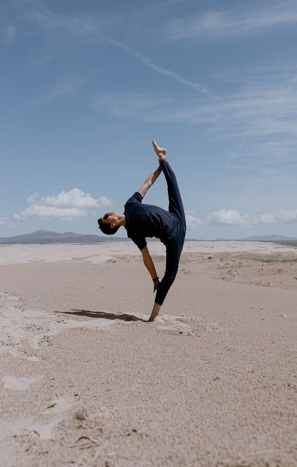 A gymnast performs a graceful backbend sequence on a vast sandy desert landscape under a bright blue sky.
