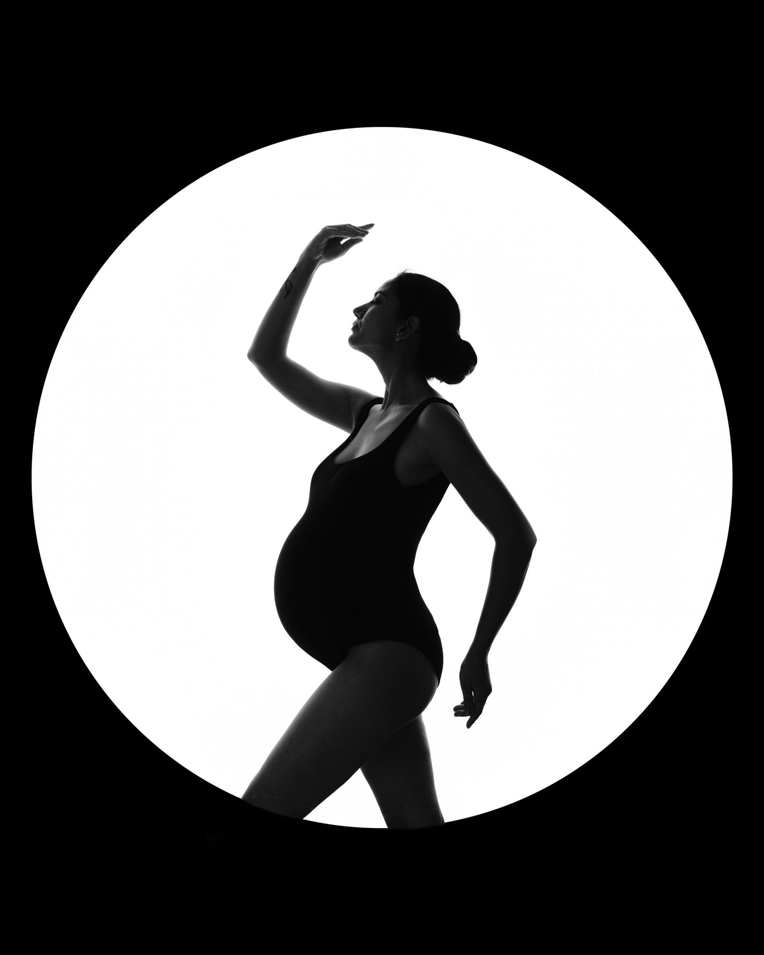 Black and white silhouette of a pregnant dancer posing gracefully against a bright circular background.