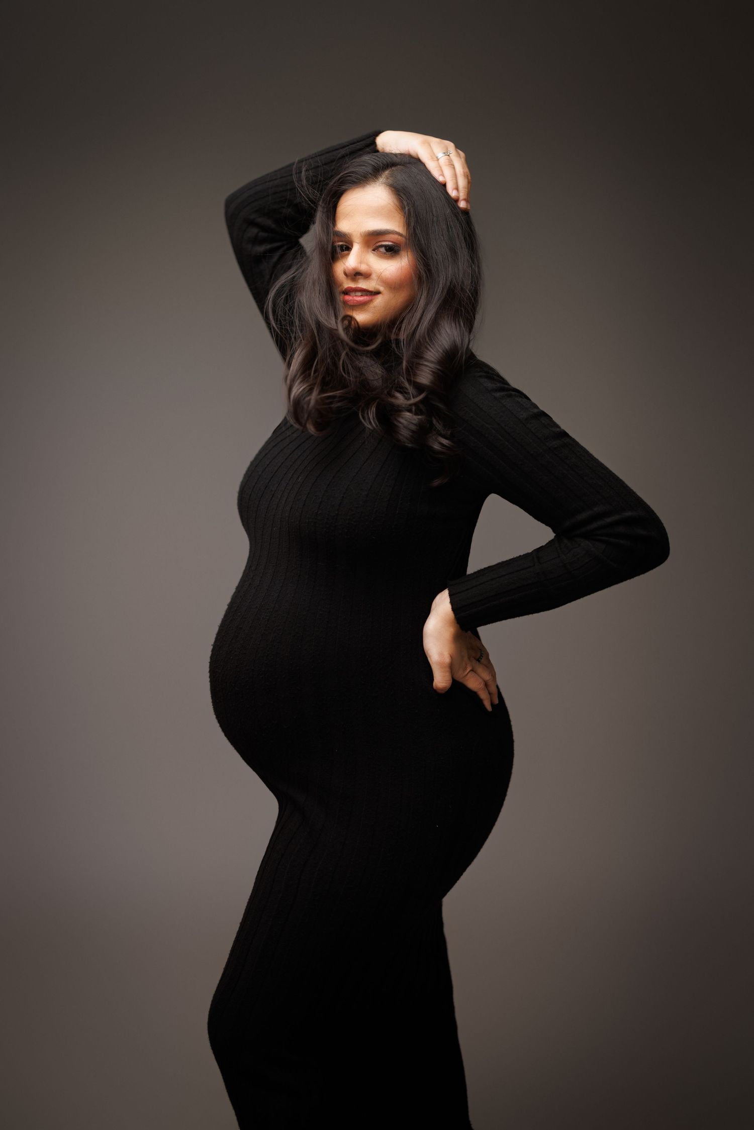 Stylish black maternity dress showcased in elegant studio portrait against dark gray background.