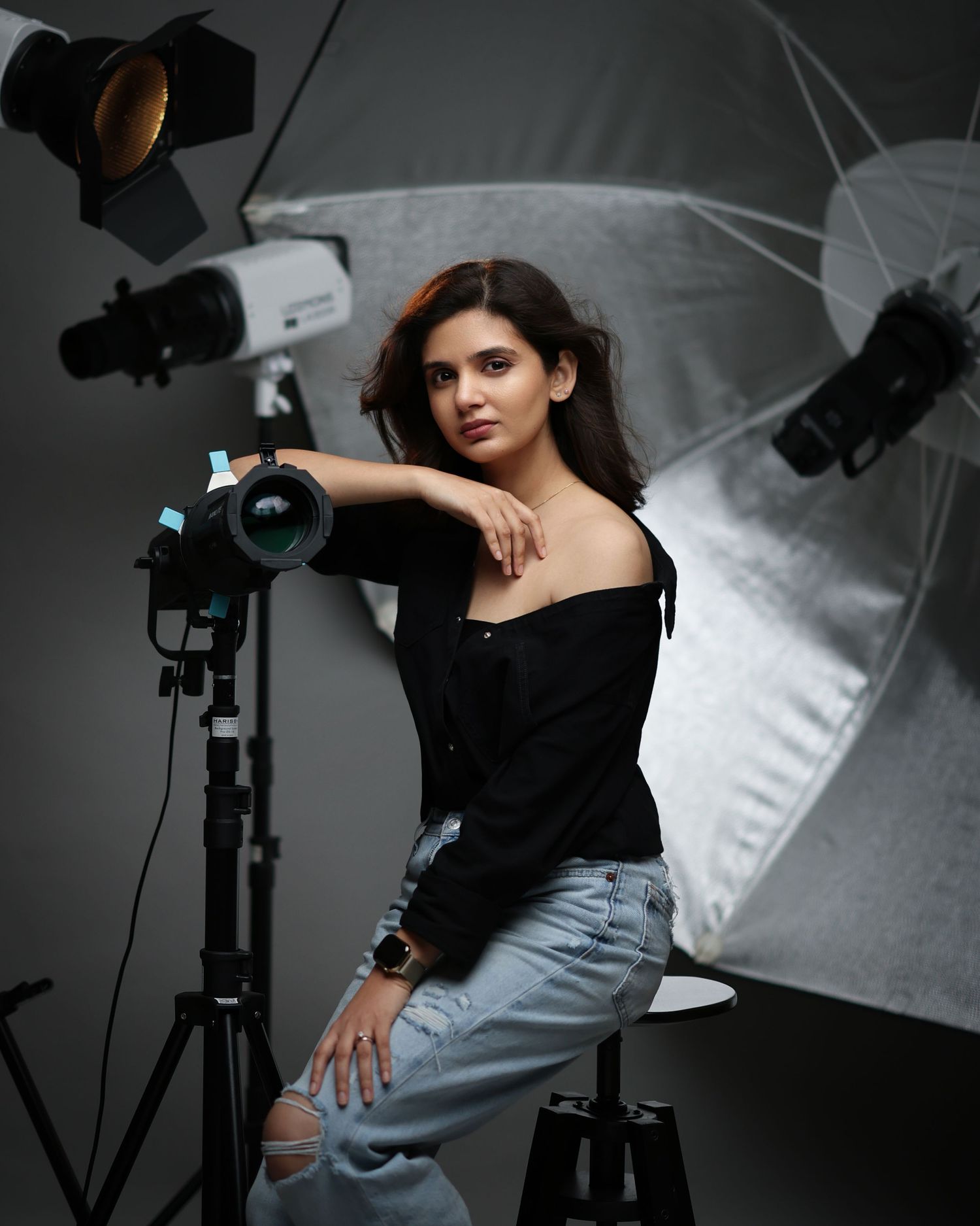 Professional photography studio setup with lighting equipment, white backdrop and a person posing in casual attire.