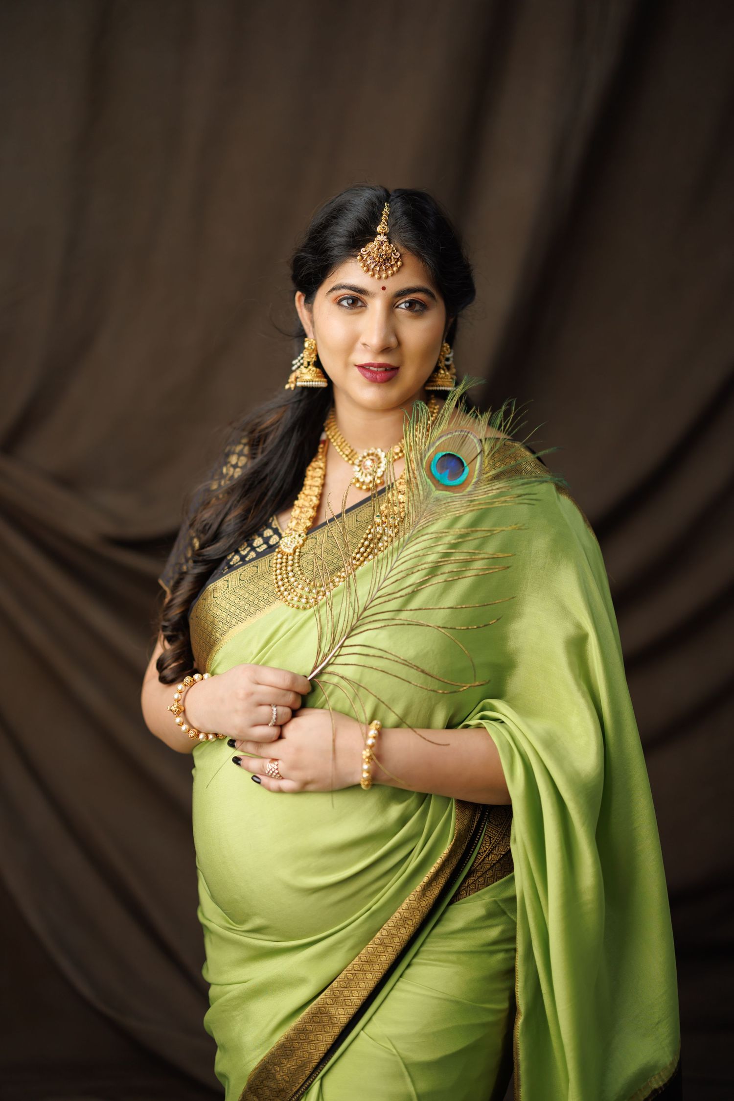 Beautiful lime green silk saree with gold border and peacock feather accent worn with traditional Indian bridal jewelry.