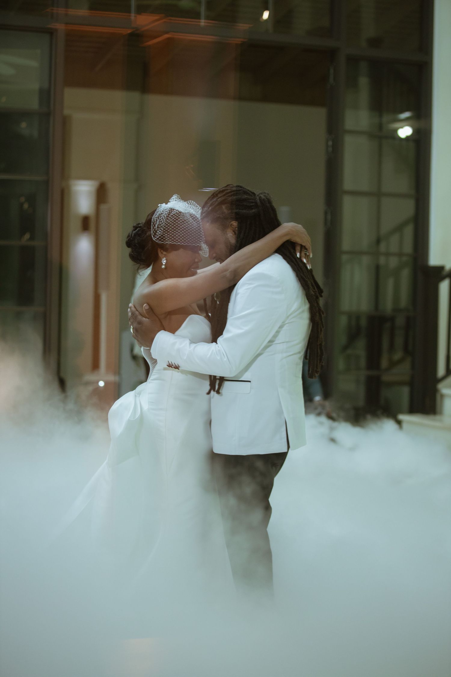 Romantic wedding couple embracing in misty indoor setting with soft lighting.