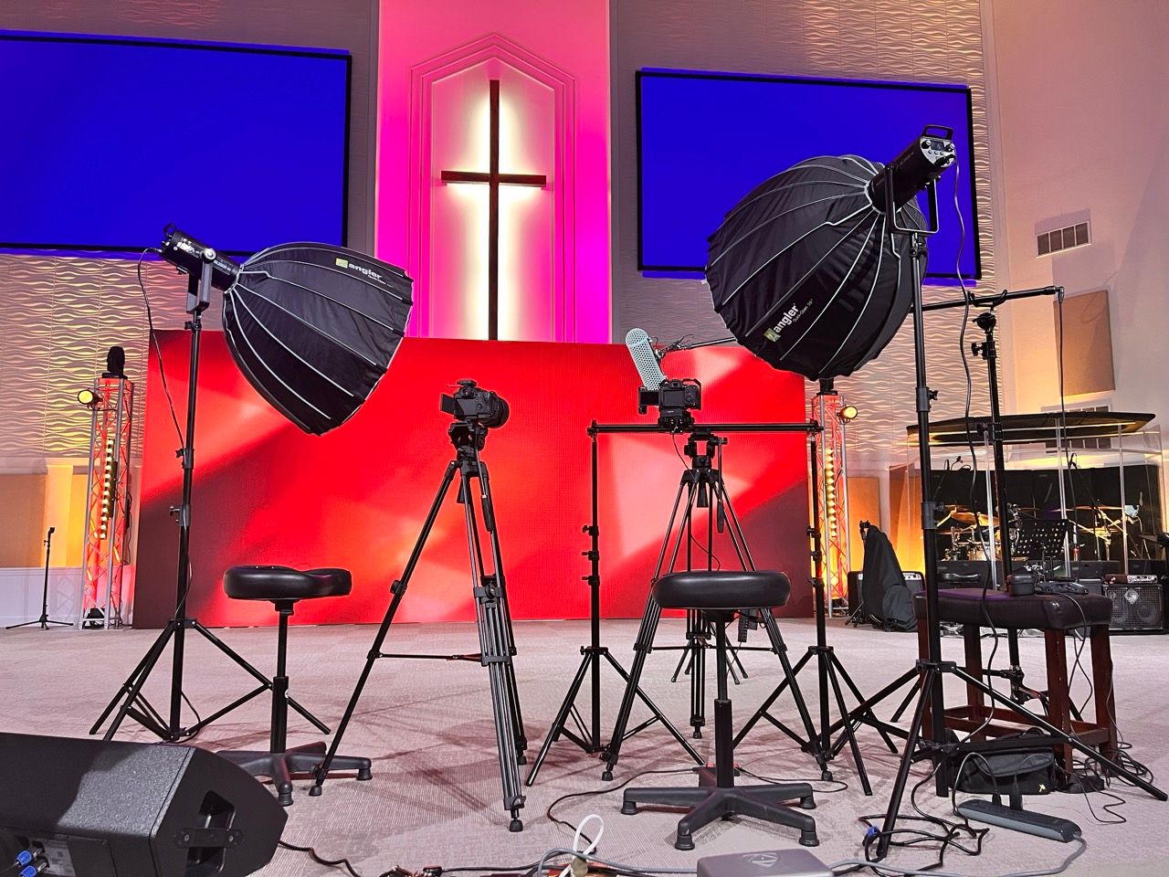 Professional photography and video equipment setup in a church sanctuary with lighting gear and a prominent illuminated cross.