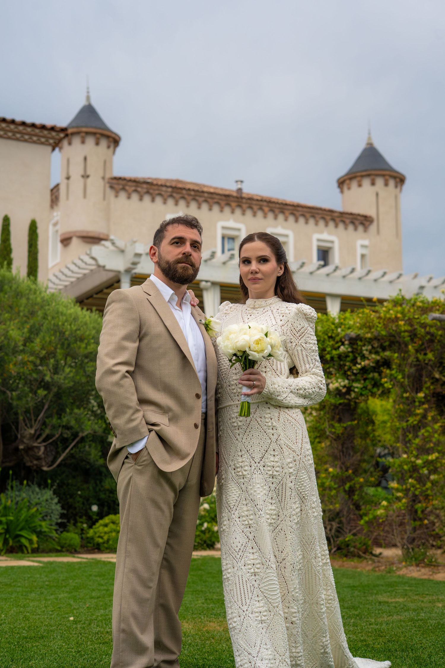 Photo d'un couple devant avec un chateau en fond pour leur mariage et la mariée à un bouquet de fleur dans les mains