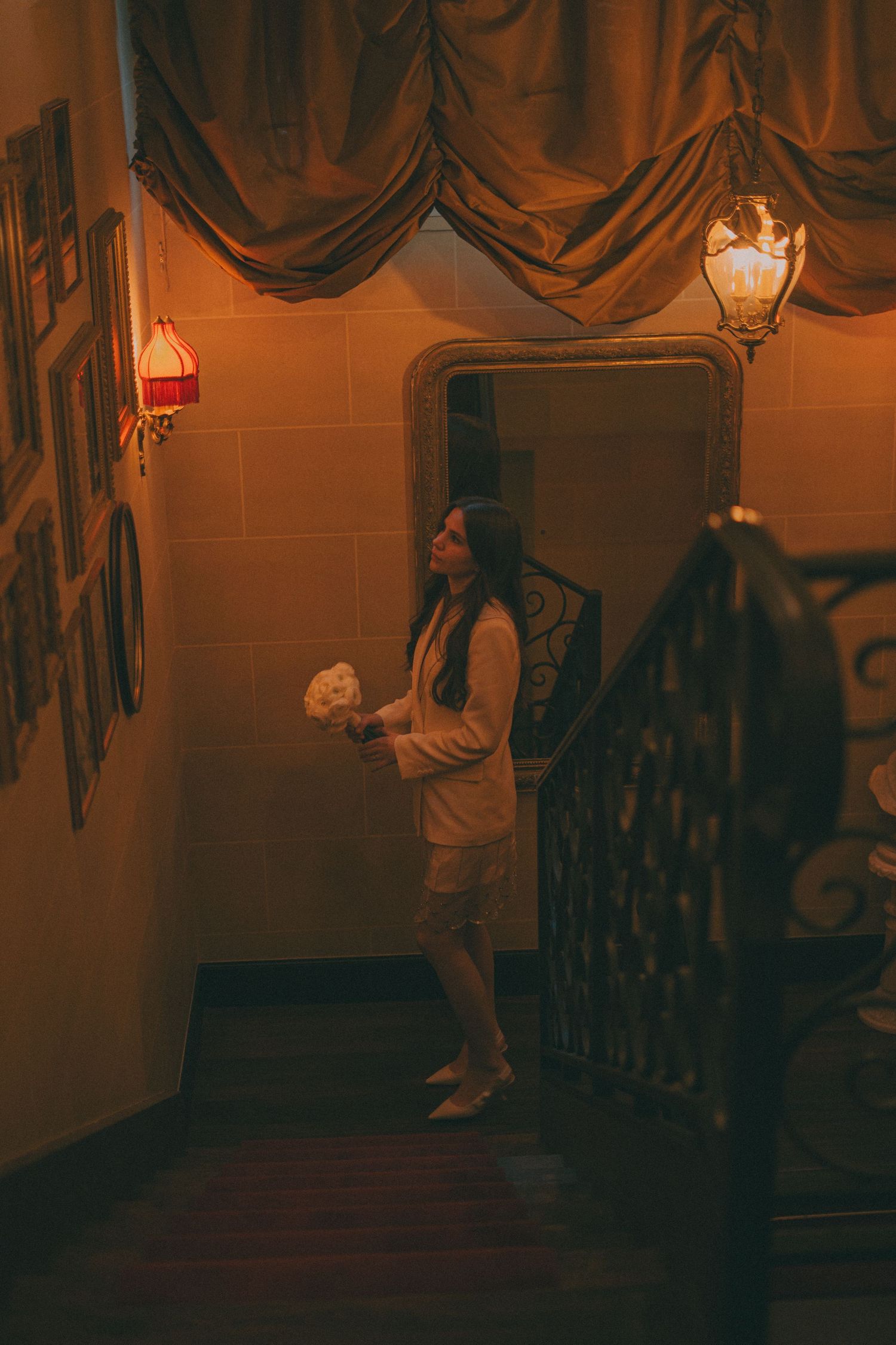 Photo d'une marié dans l'établissement Revka Paris dans les escalier tenant son bouquet dans les mains et regardant les cadres photos