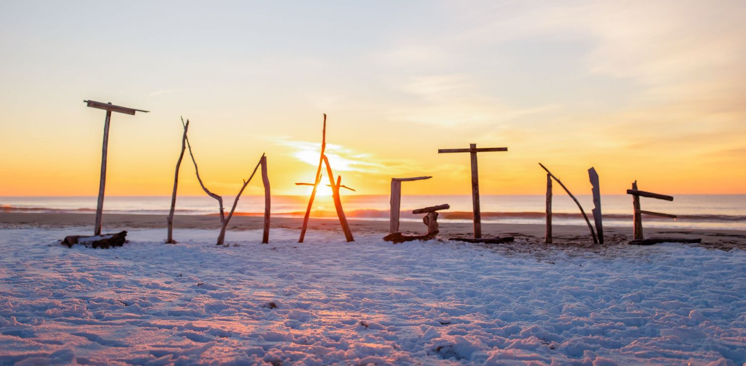 A series of snow-covered wooden fence posts silhouetted against a vibrant orange winter sunset.