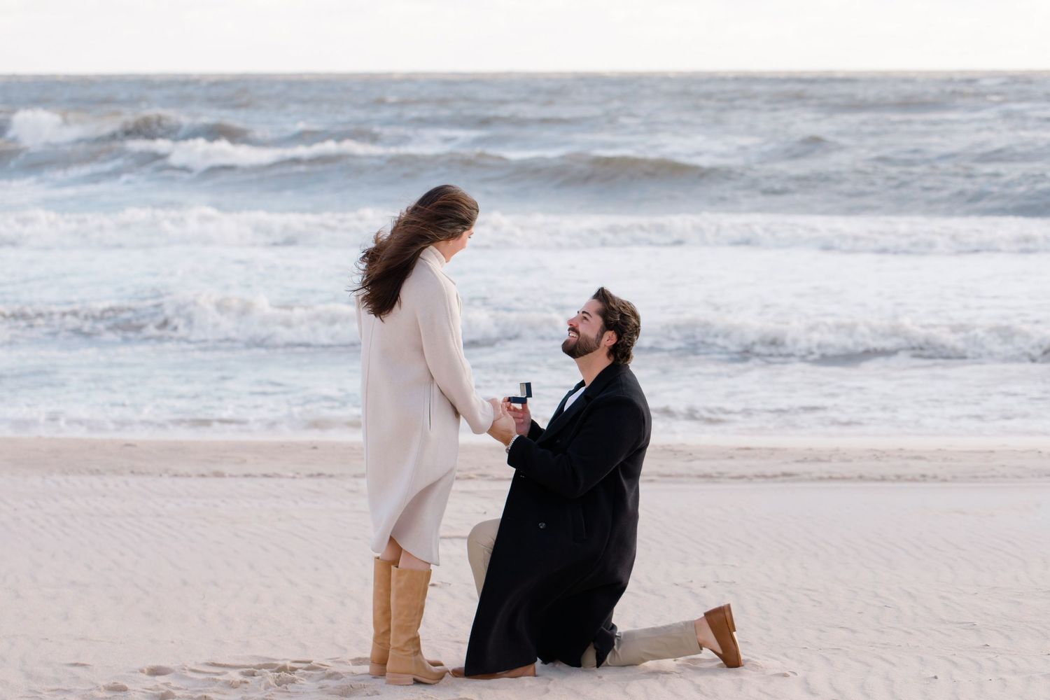 A romantic Hamptons beach proposal scene with crashing waves in the background during sunset.