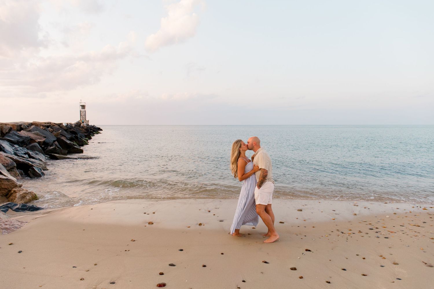 A person performs yoga poses on a sandy beach at sunset with the ocean and rocky coastline in the background.