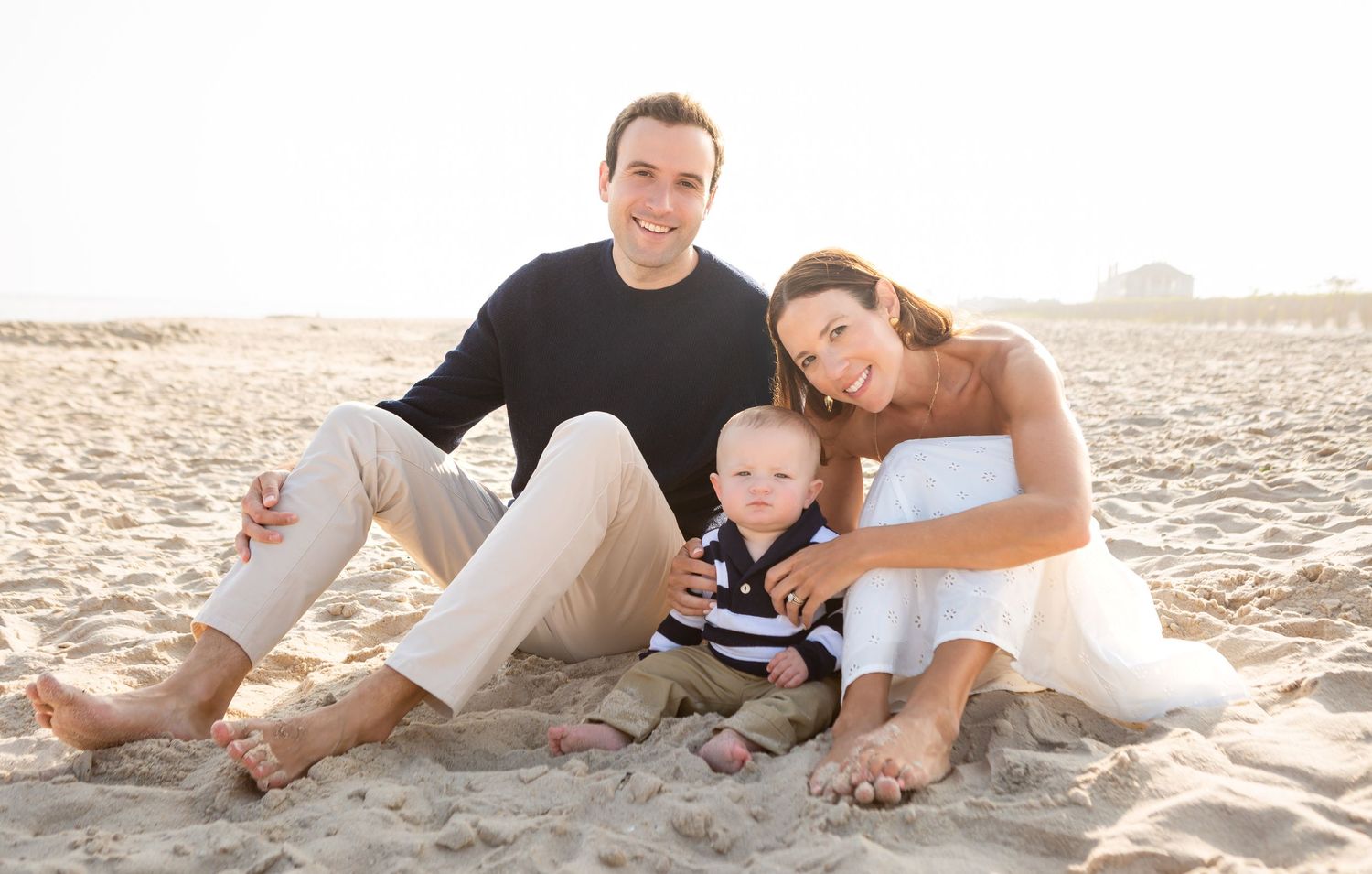 Family wearing white clothes relaxing together on sandy beach during golden hour sunset.