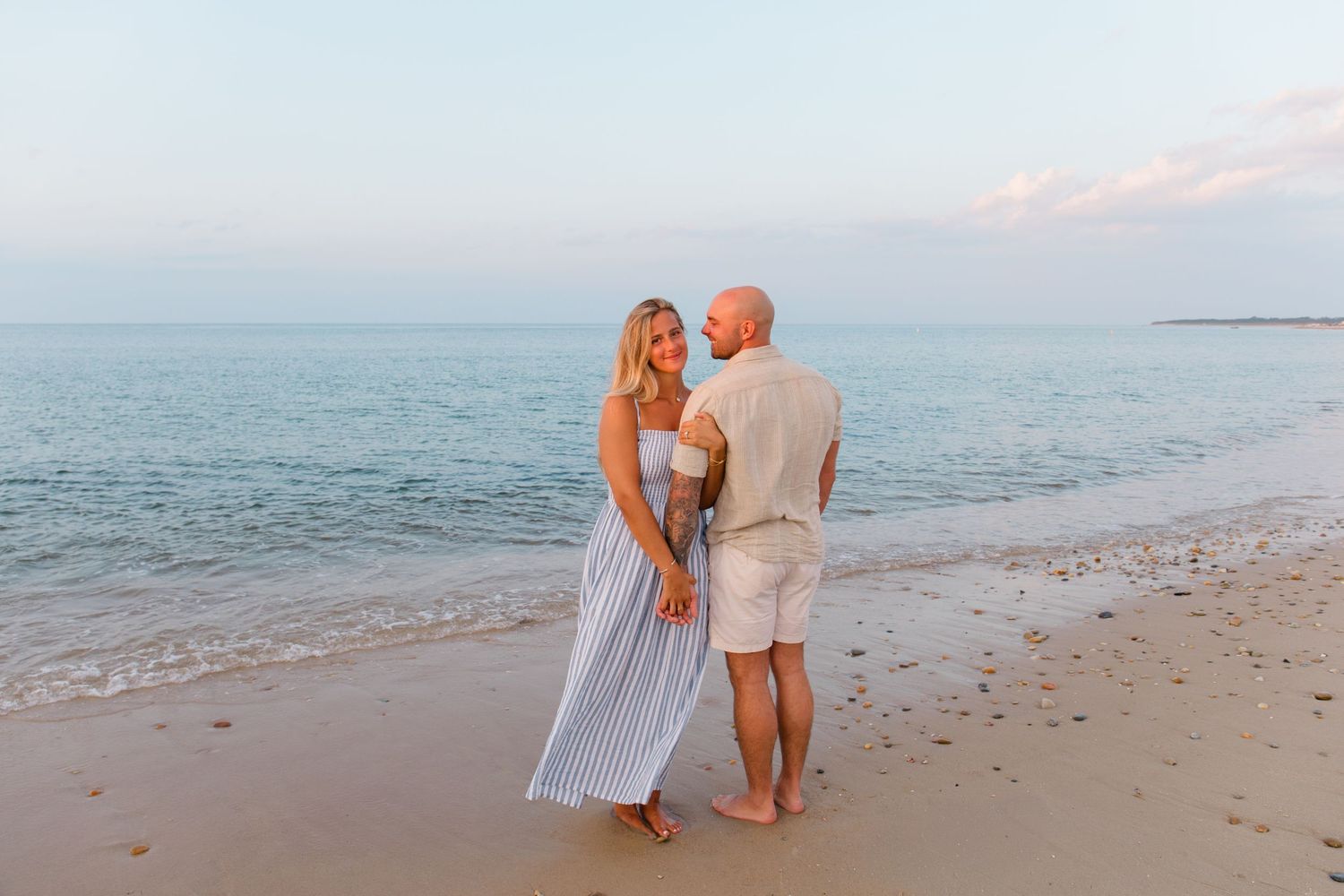 Two people share an intimate moment together on a peaceful beach at sunset with ocean waves in the background.