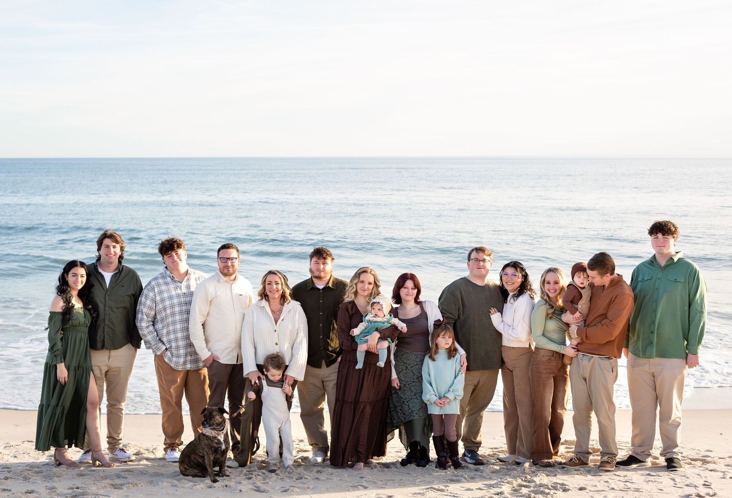 A group of people standing together in a line on a sunny beach wearing casual attire.
