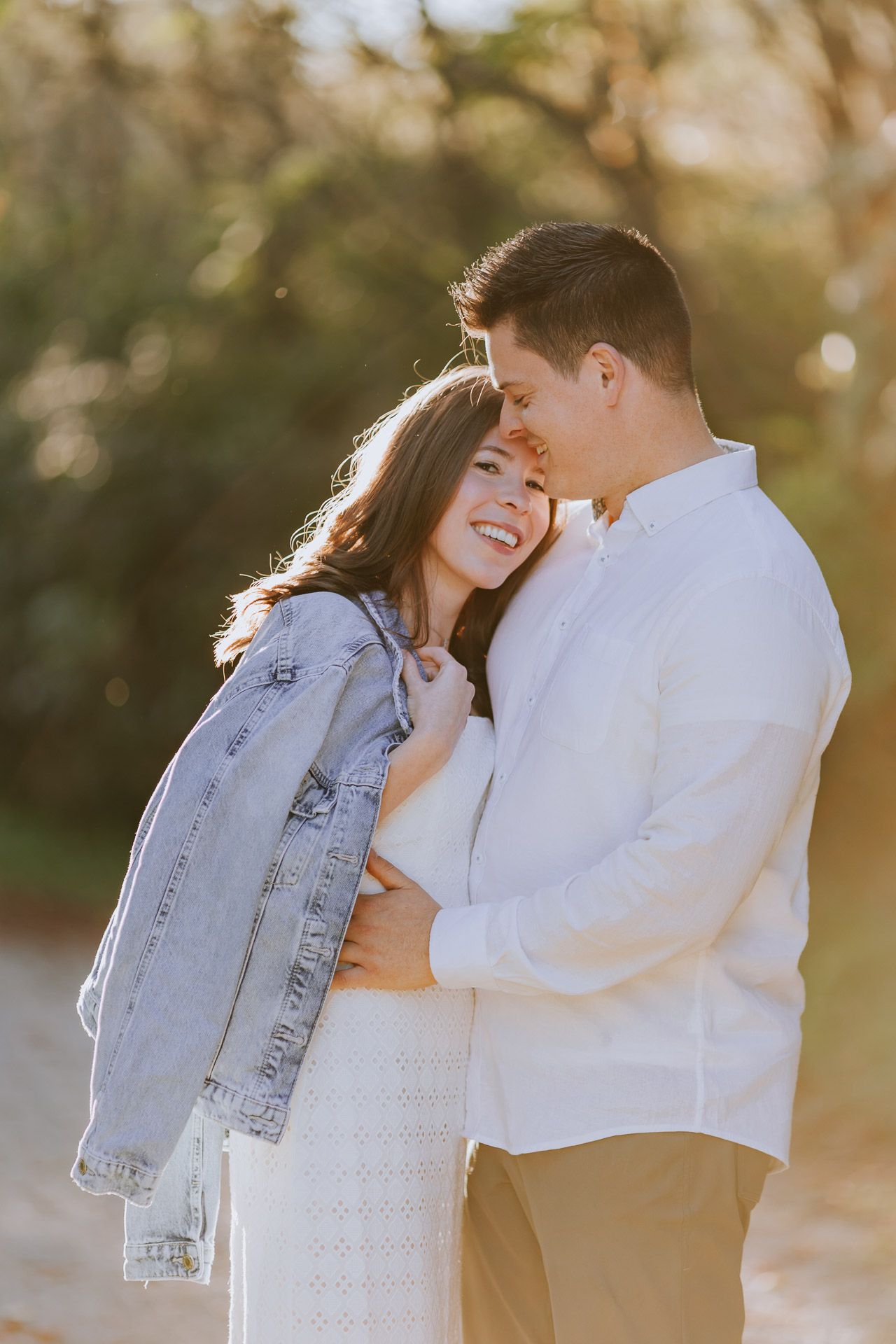 A romantic couple shares intimate moments in golden sunlight while wearing white and denim clothing.