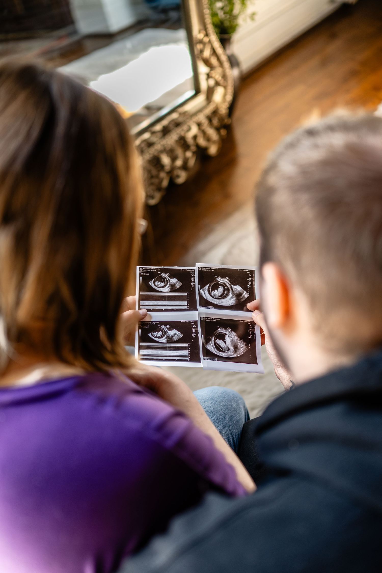 Couple looking at ultrasound photos together, expecting parents reviewing baby sonogram images at home.