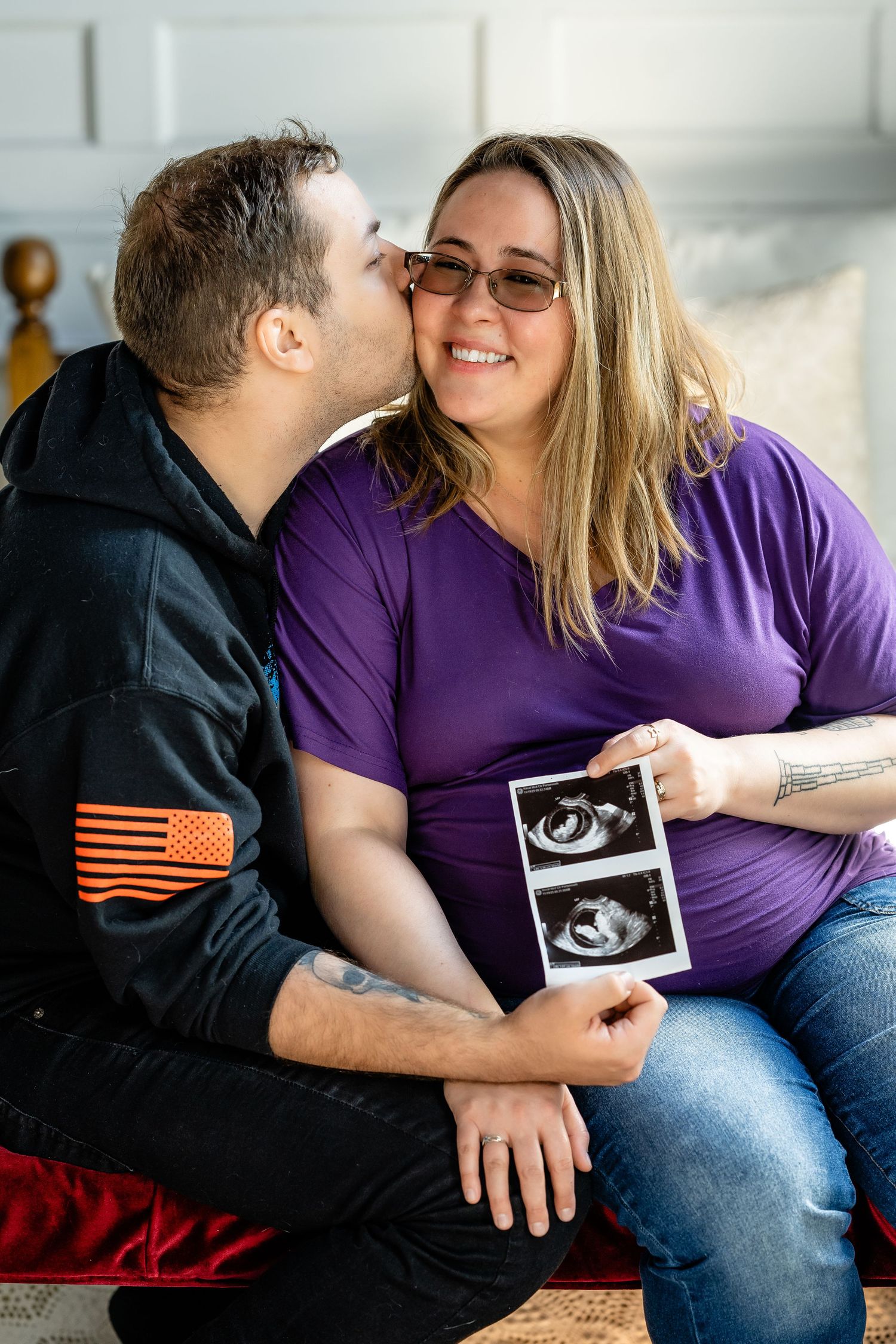 A couple shares a tender kiss while holding an ultrasound photo, announcing their pregnancy together.