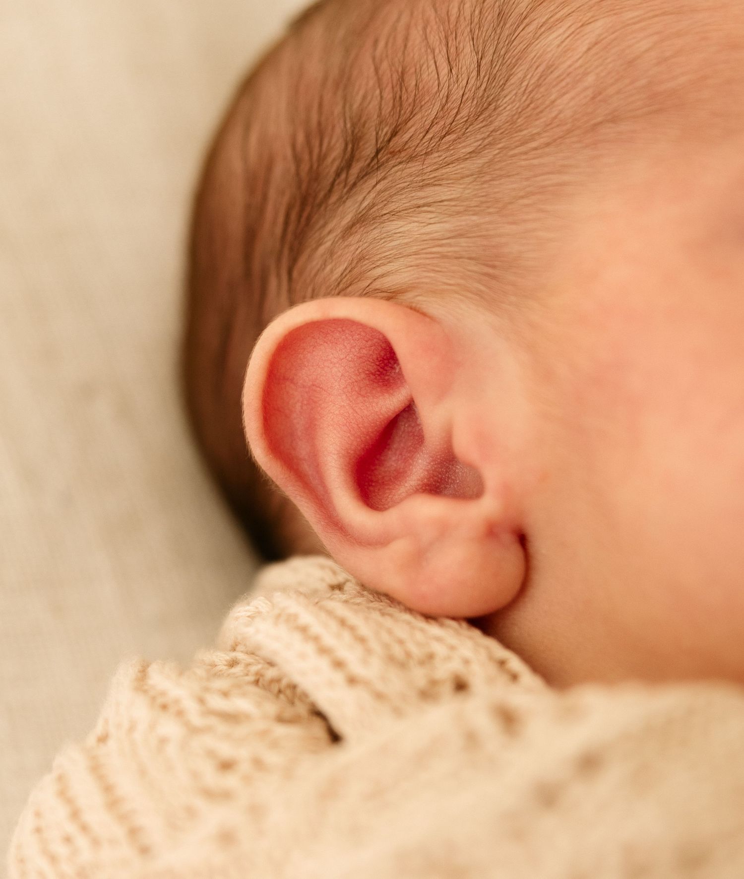 Close-up of a sleeping newborn baby's tiny ear and soft skin in warm light.