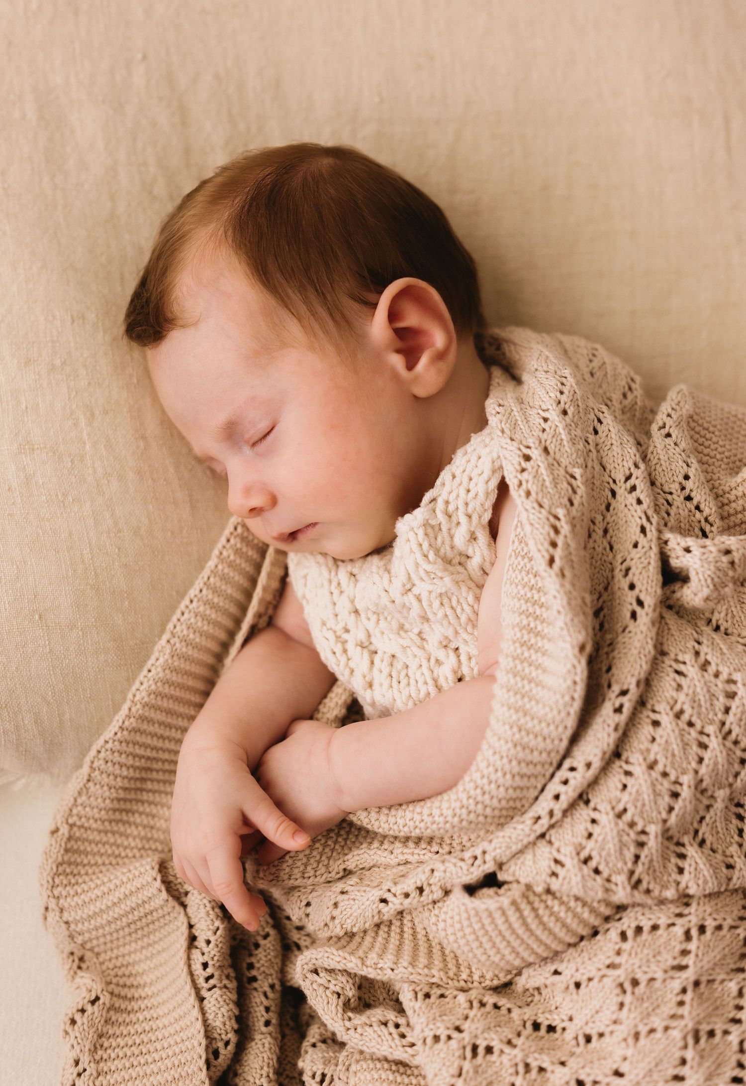 Peaceful newborn baby sleeping wrapped in a cream knit blanket.
