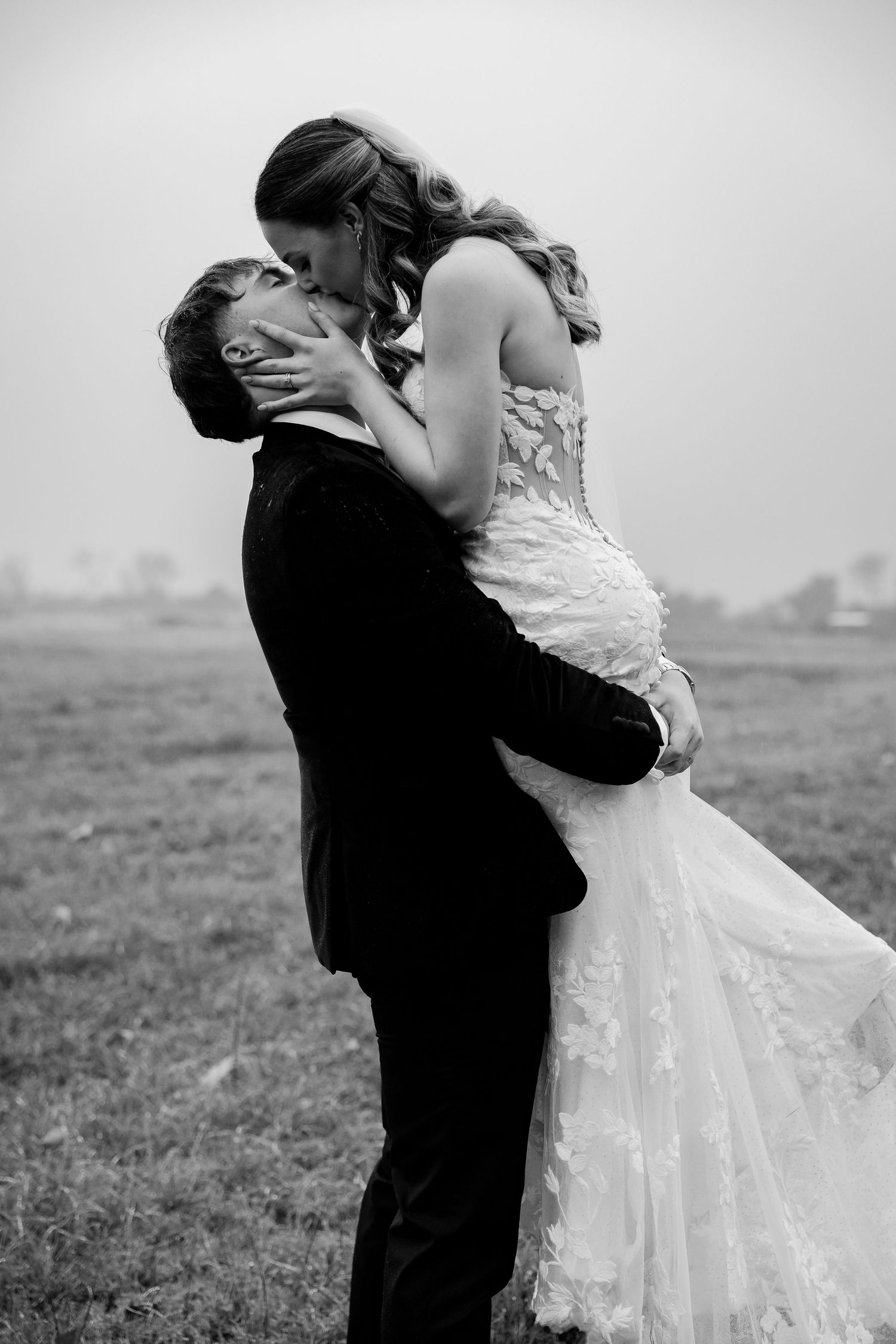 Black and white romantic photo of a groom lifting his bride for a passionate kiss outdoors.