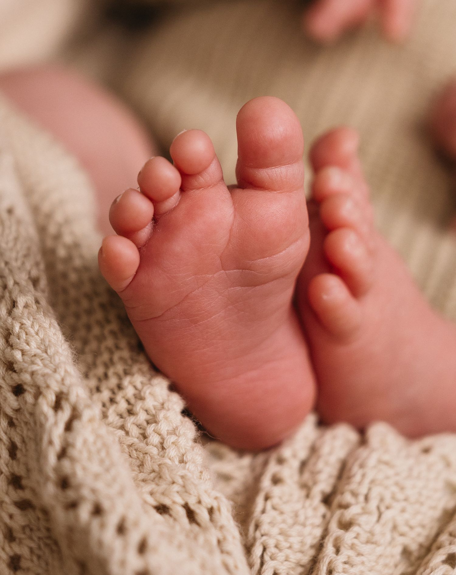 Close-up of newborn baby feet resting on a soft beige knitted blanket.