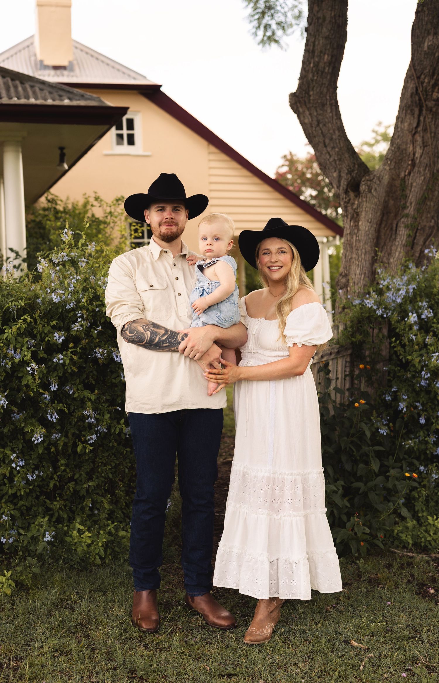 Couple in matching black cowboy hats holding toddler in garden setting.