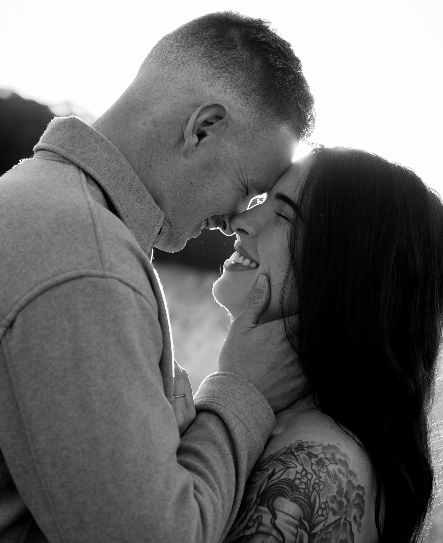 Black and white photo of tattooed couple embracing and smiling intimately.