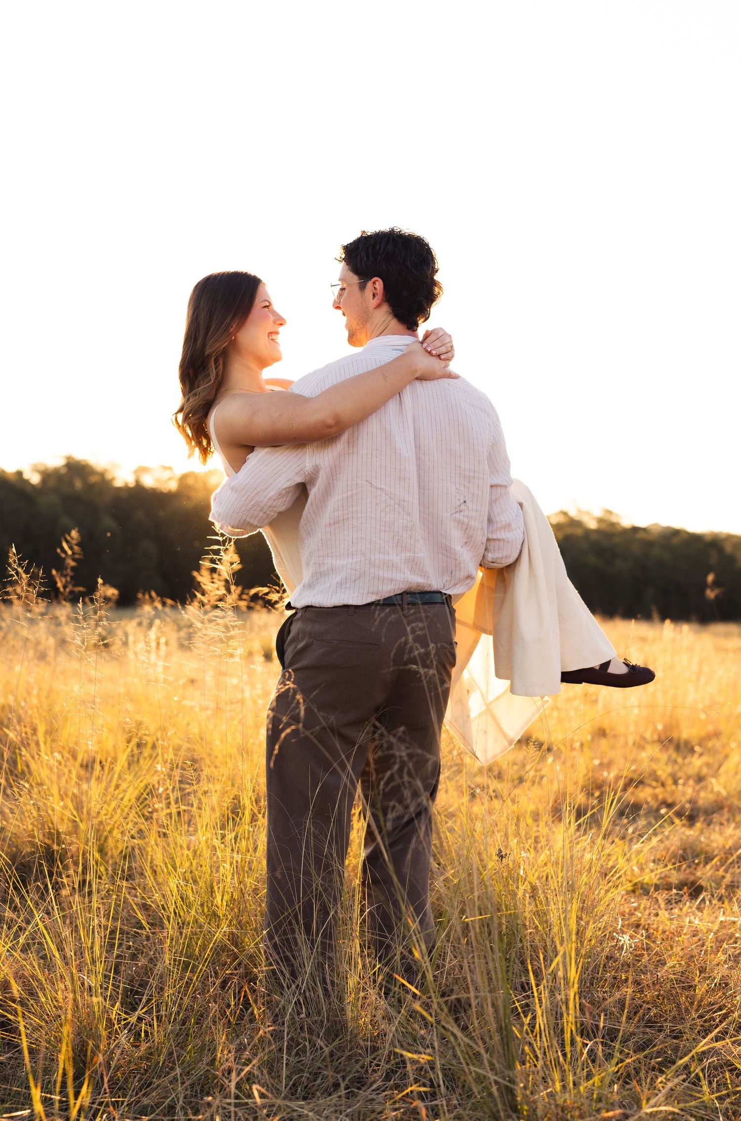 Man lifting woman in golden sunset field during romantic couples photo session.