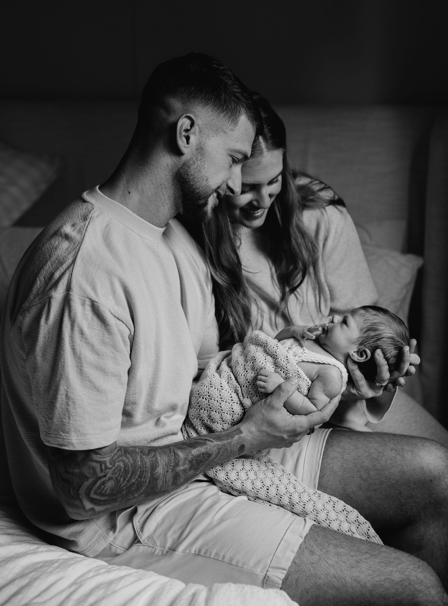 Tattooed father and mother admire their newborn baby in black and white photo.