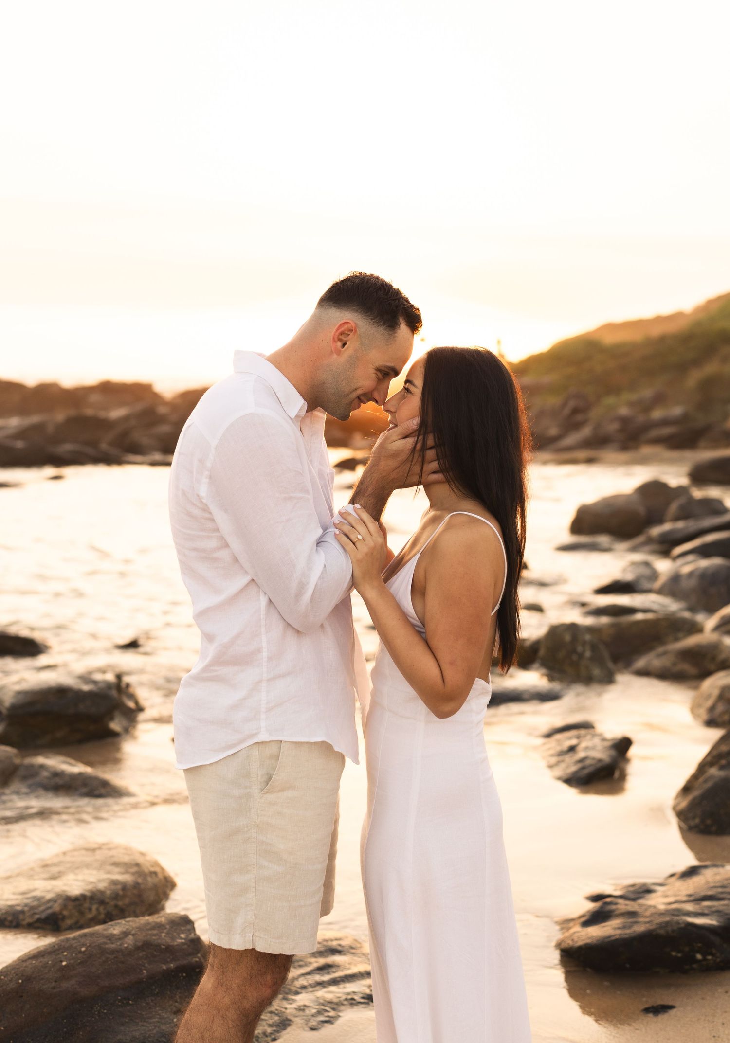 Couple sharing romantic moment on rocky beach during golden sunset hour.