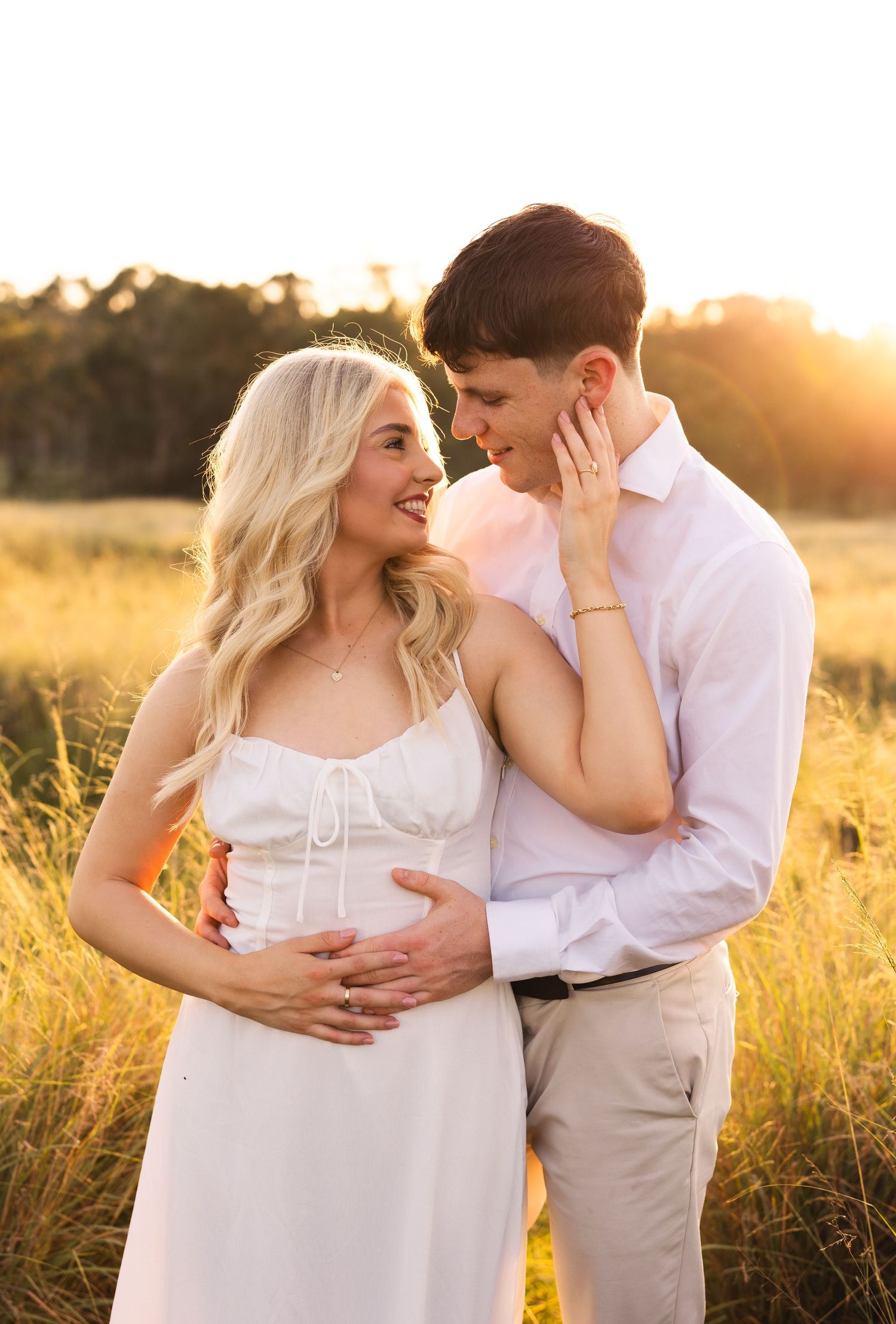 Happy couple sharing a tender moment in a golden field at sunset, woman touching mans face gently.