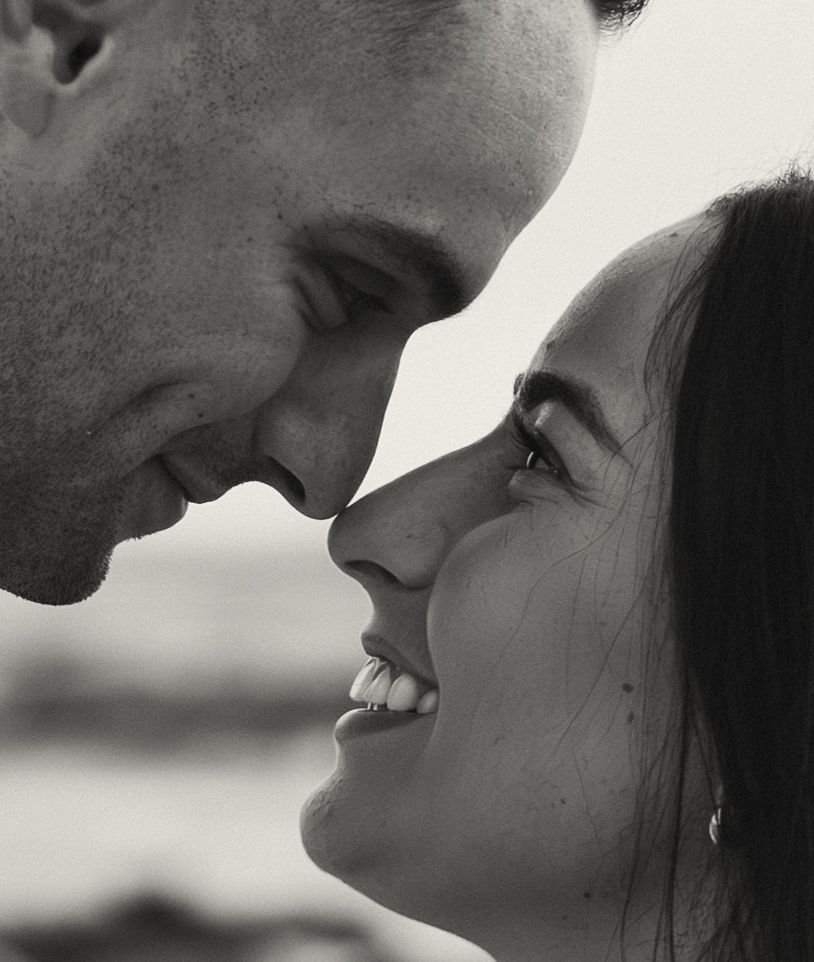 Black and white close-up of a couple almost kissing, foreheads touching, smiling intimately.